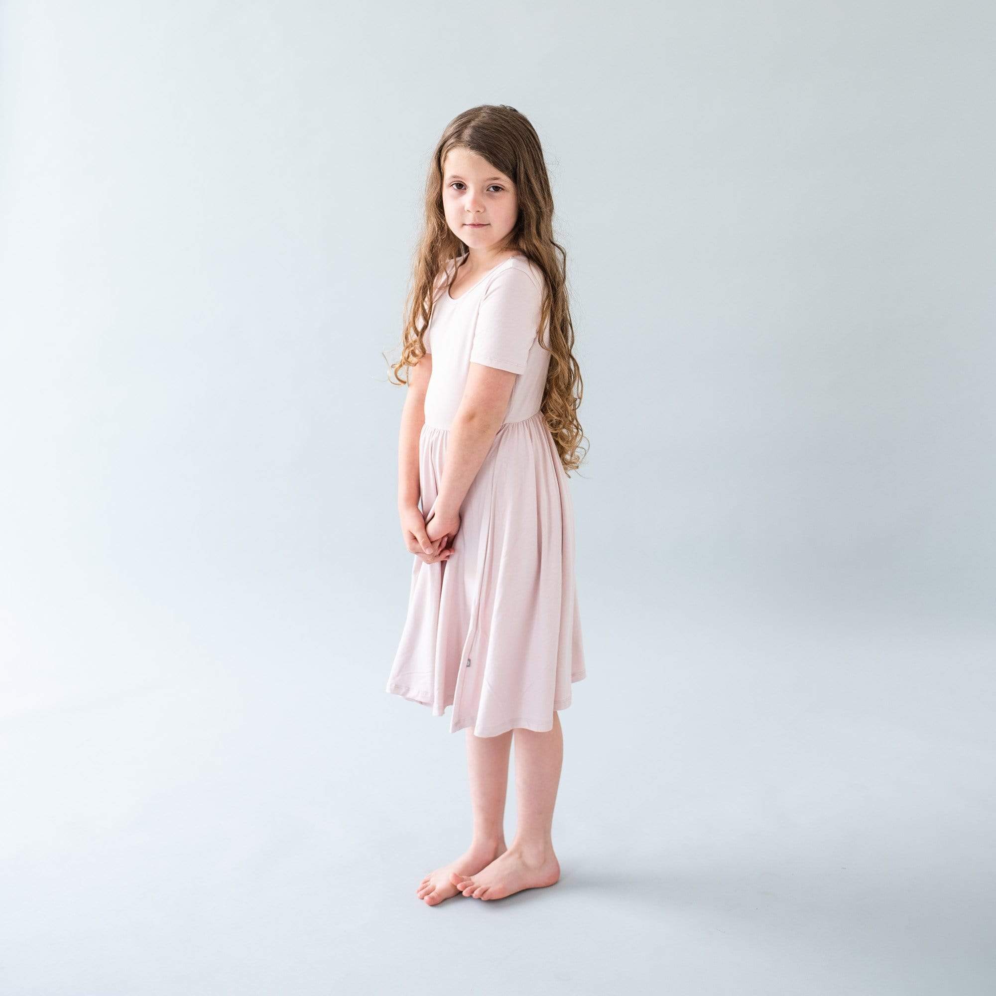 Child standing in a gray room while wearing a Twirl Dress in Blush