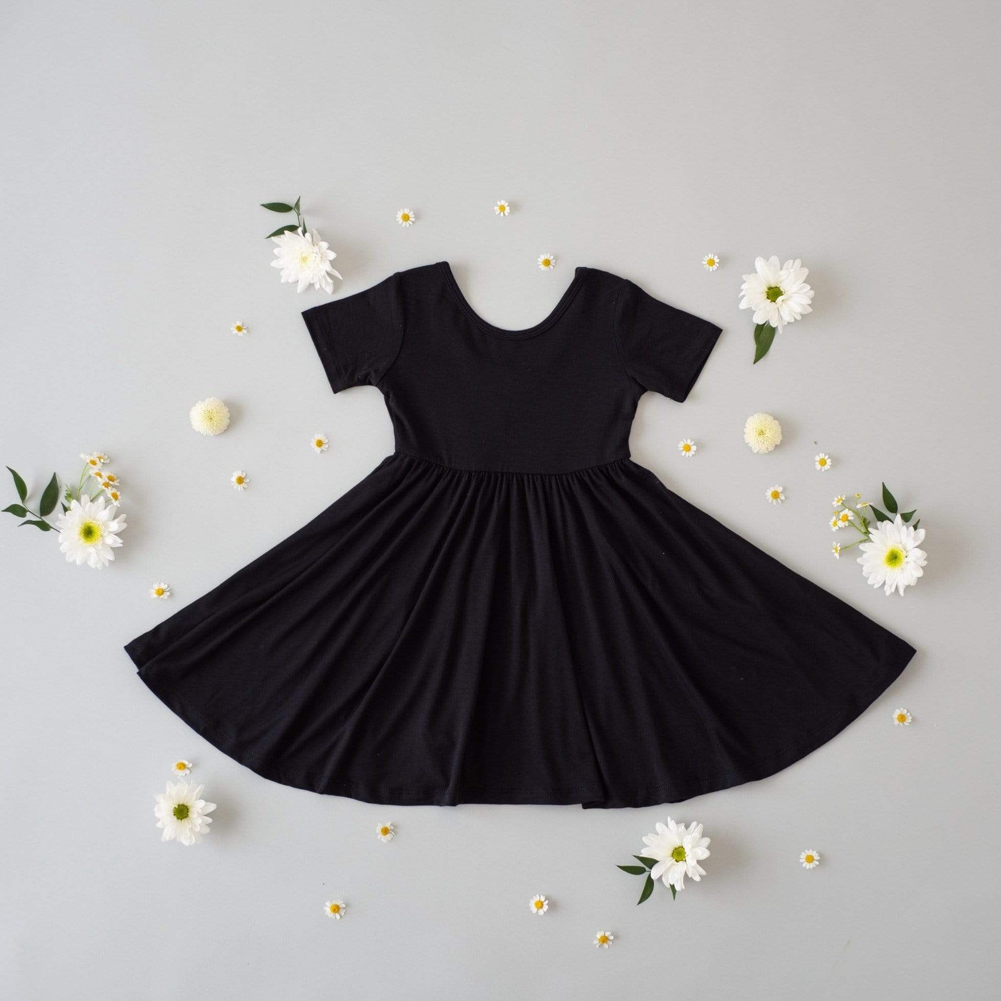 Flat lay of Twirl Dress in Midnight on a gray surface with white flowers spread around it