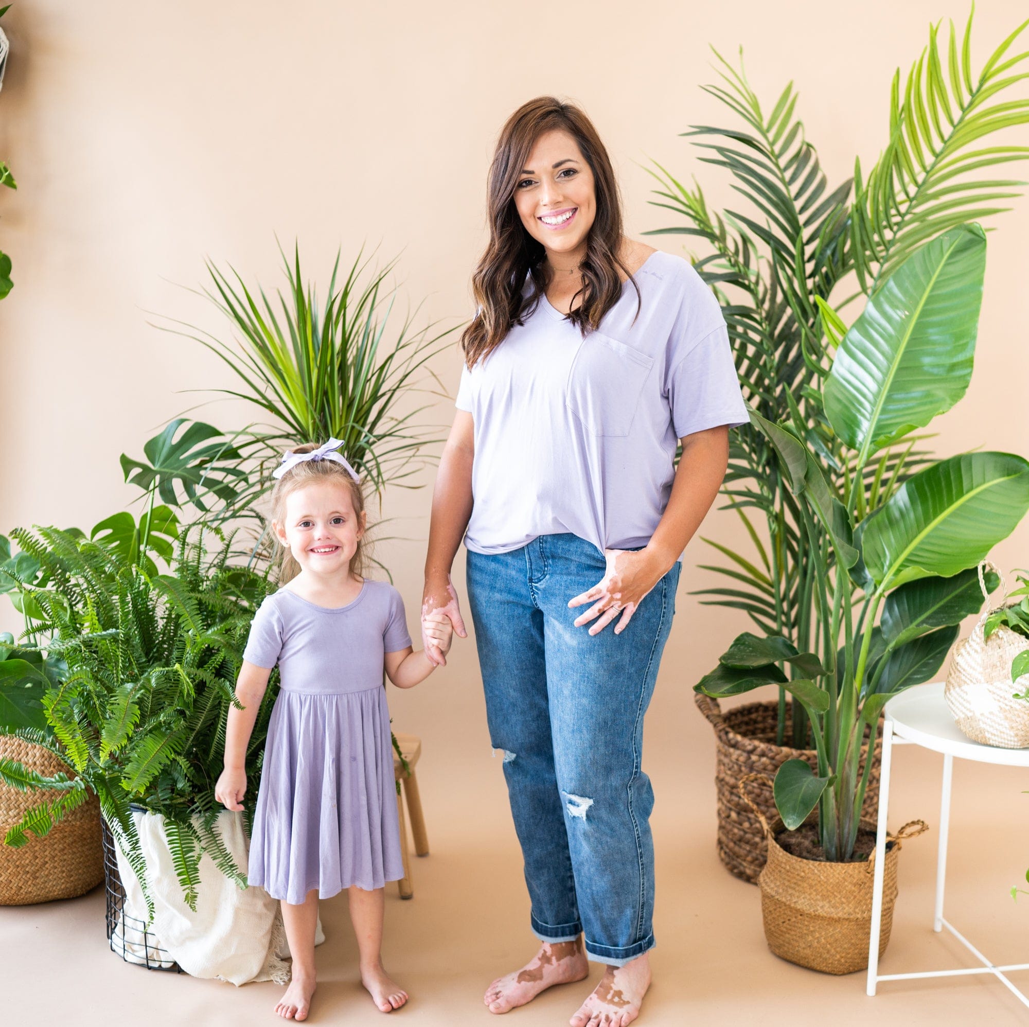 Mom and daughter holding hands and wearing matching Kyte Baby outfits in Taro with plants surrounding them