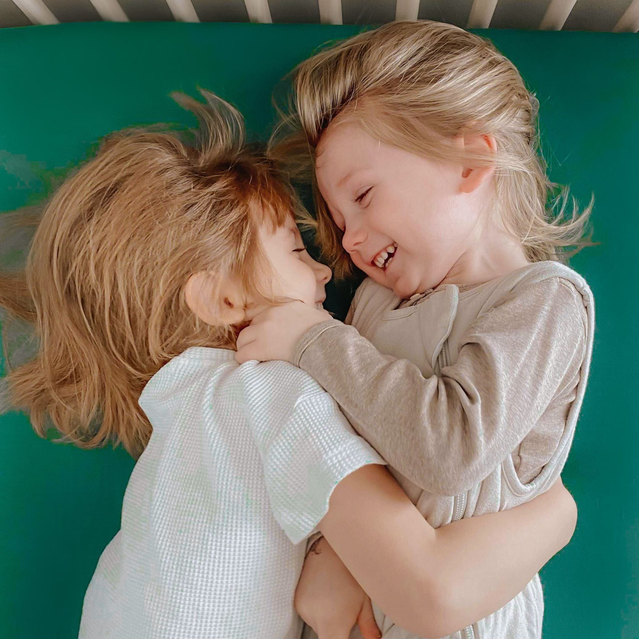 Kids laying on bed with Corner of Kyte Baby Twin Sheet in Emerald