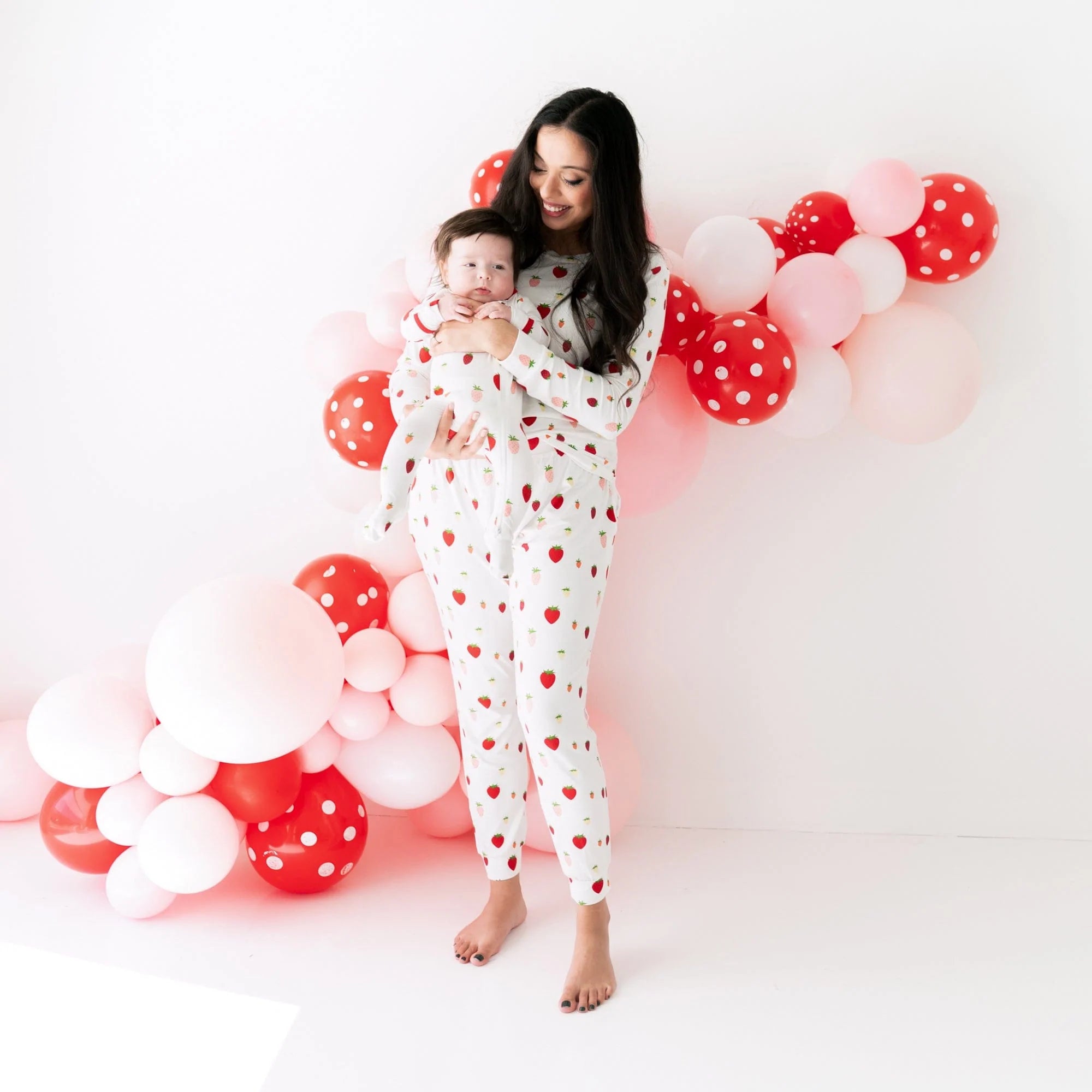 Mom and infant wearing Kyte Baby matching family pajamas in Strawberry