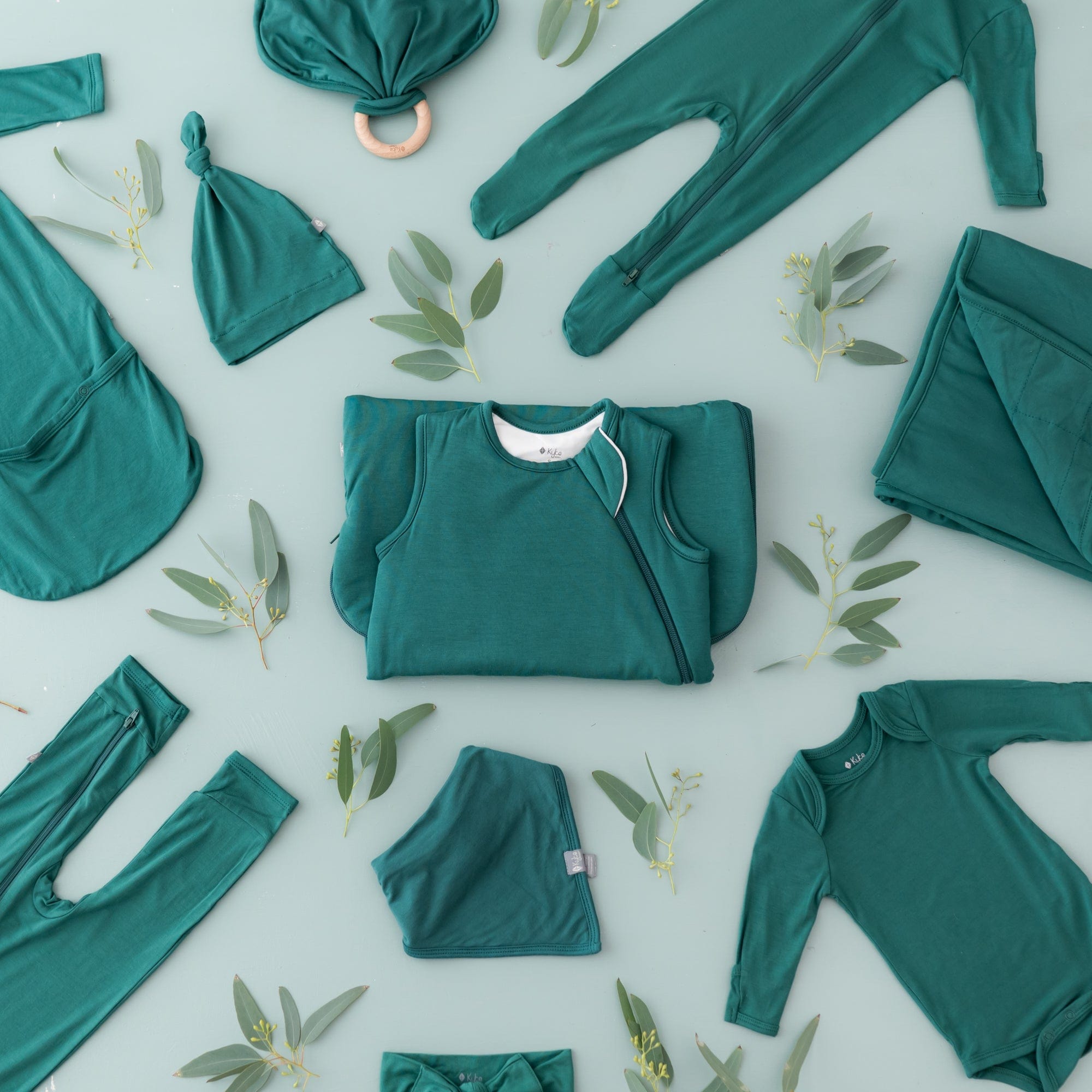 Flat lay of multiple Kyte Baby styles in Emerald on a sage surface