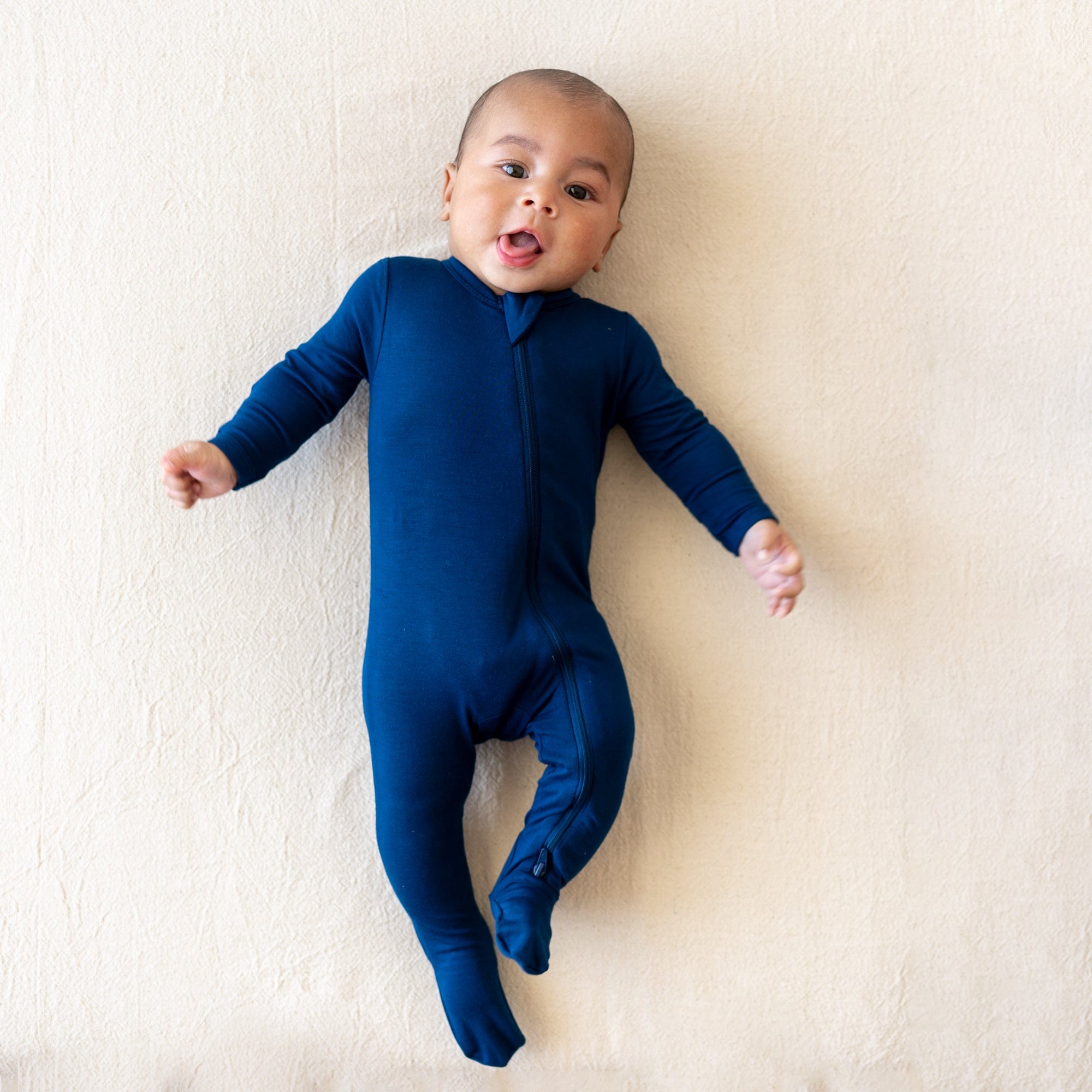 Infant laying down with tongue sticking out wearing the Zippered Footie in Tahoe