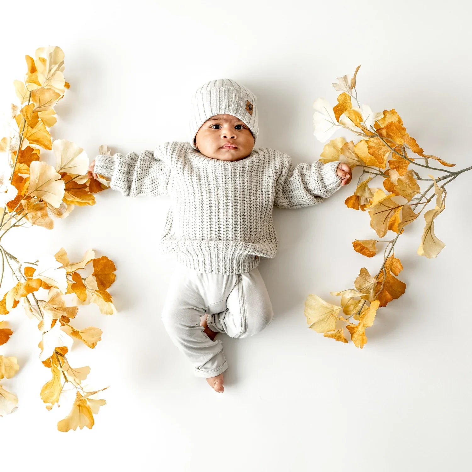 Baby in Cozy Kyte Baby Sweater and Beanie with Fall Leaves