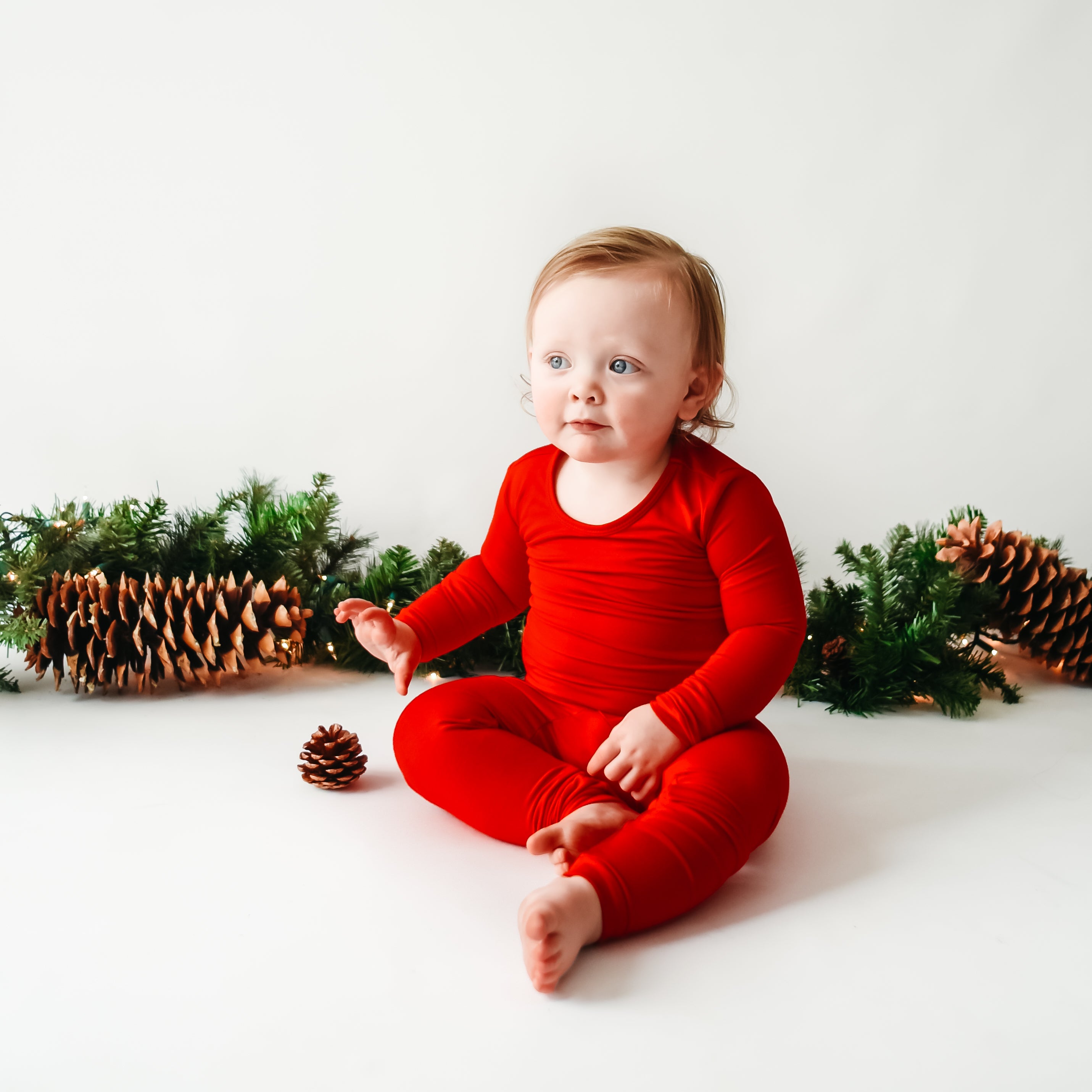 baby wearing crimson kyte baby pajamas with a pinecone garland in the background