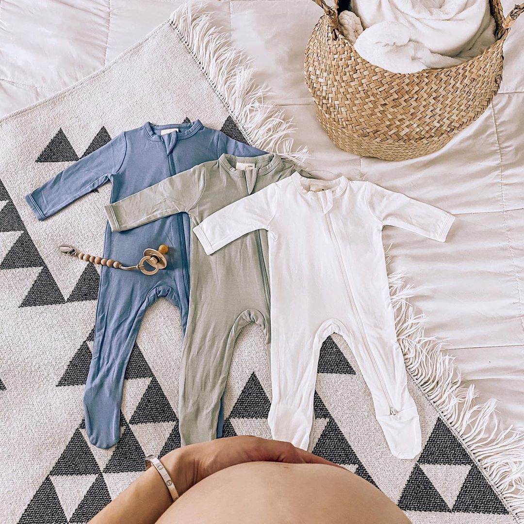 mom standing over kyte baby footies on the bed