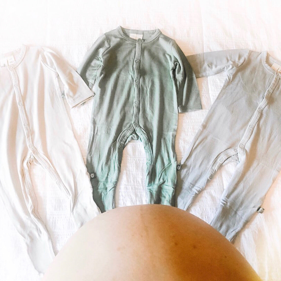 Mom looking down over her baby bump at three sets of pajamas