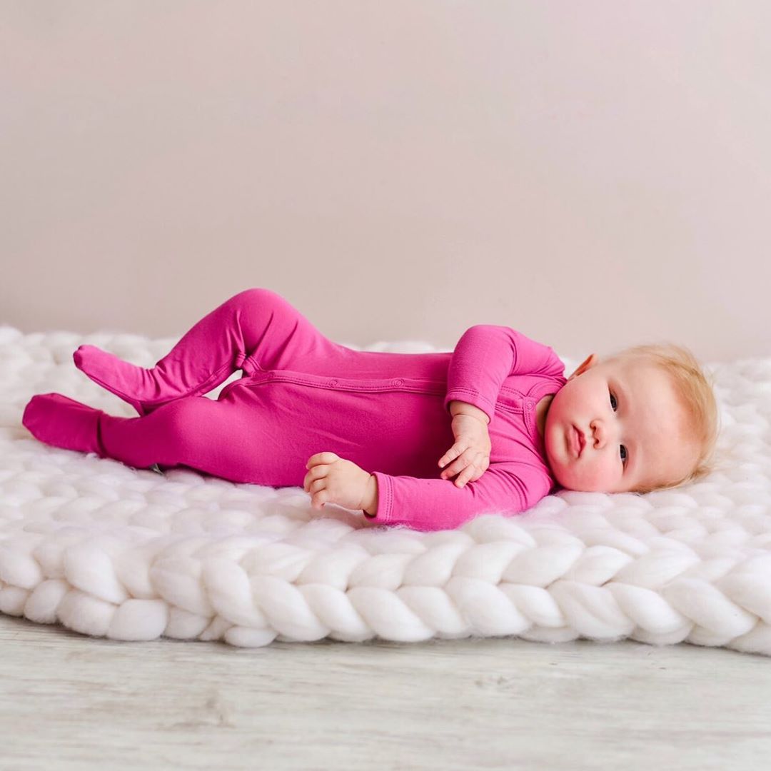 Baby rolling on a blanket wearing raspberry pink footies