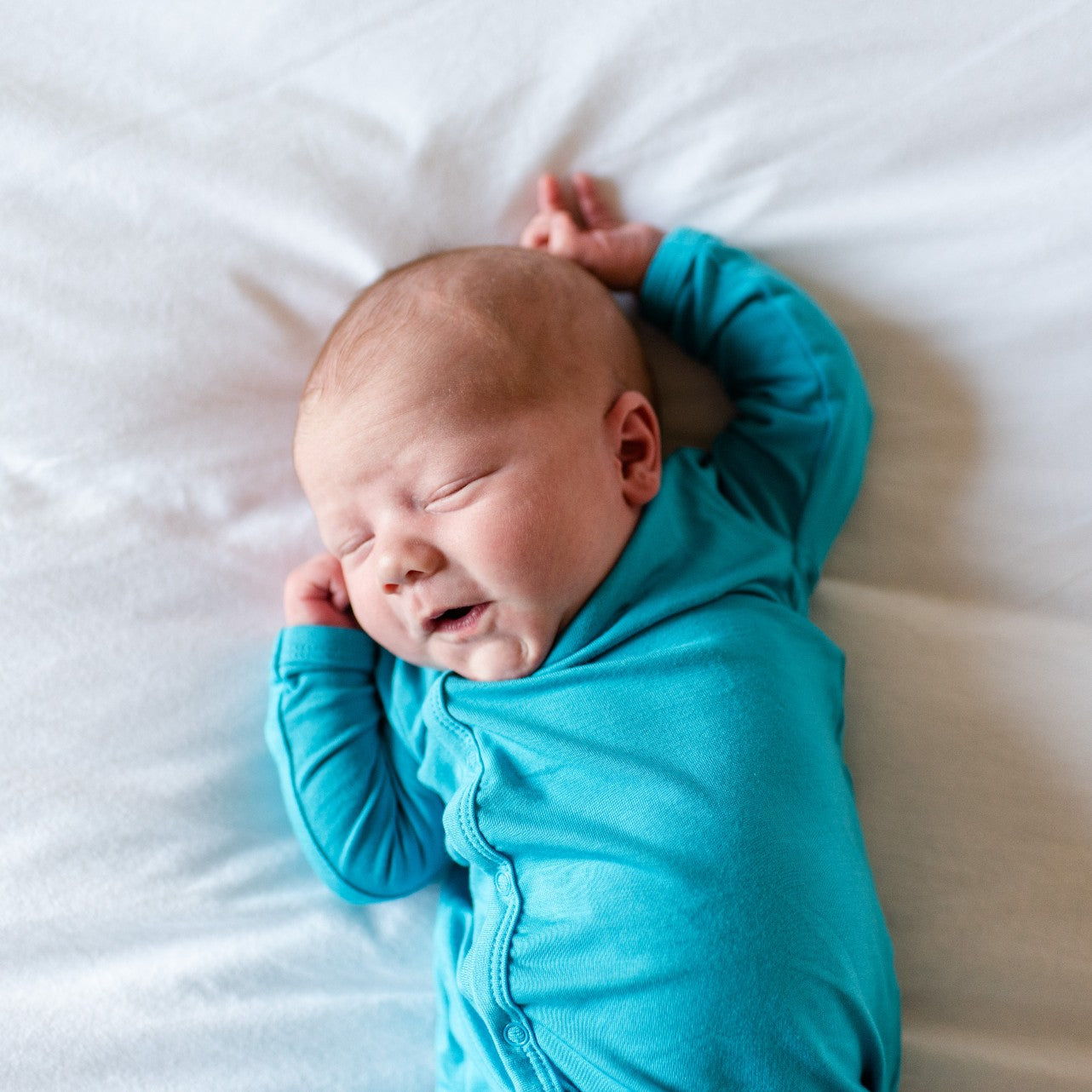 newborn baby laying down with arms above head
