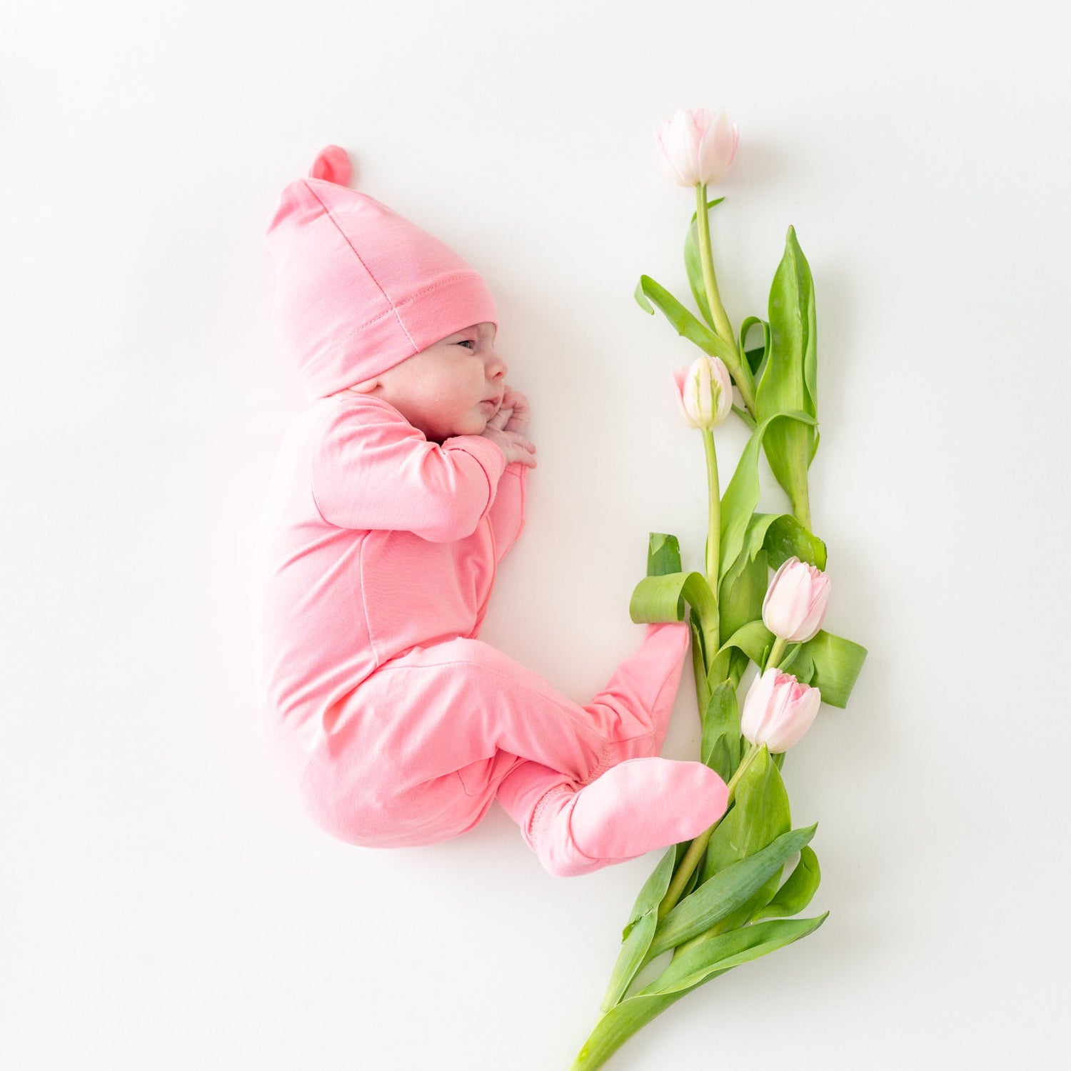 Newborn baby resting on her side in romper pajamas and a knotted cap