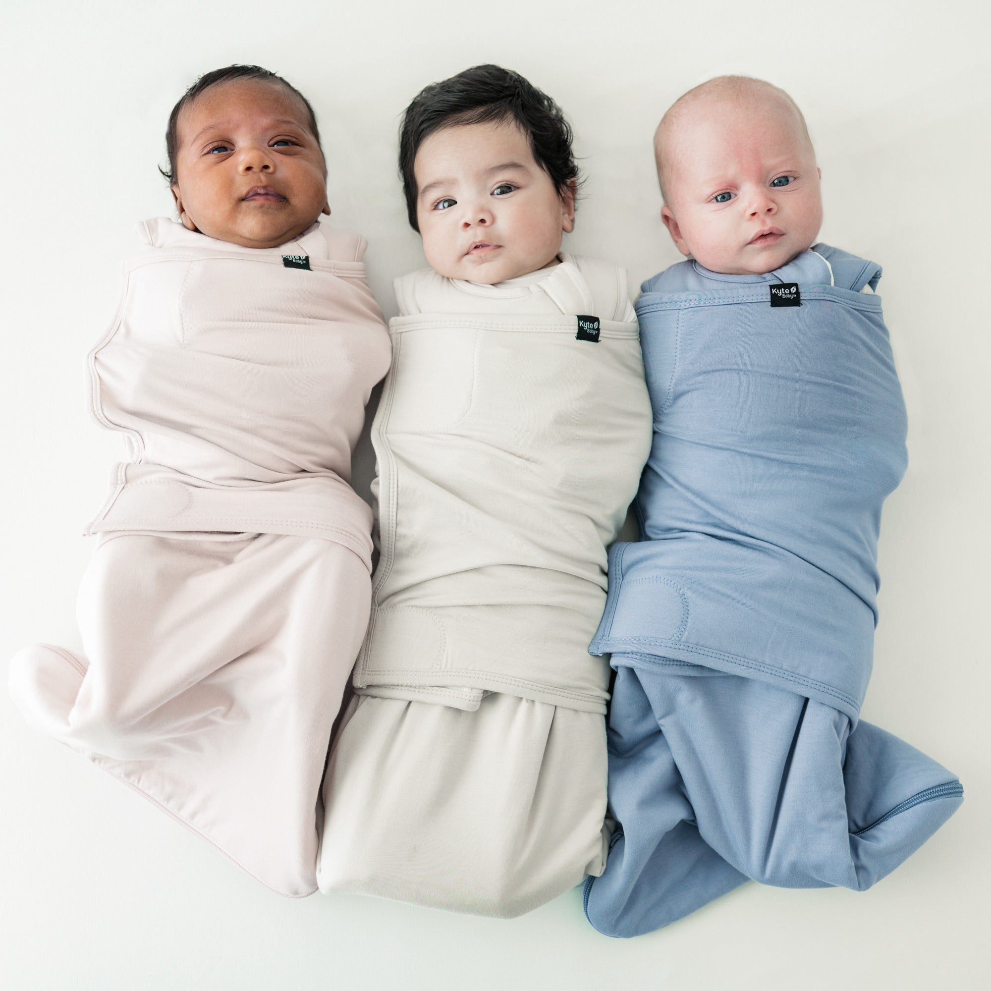 three newborns laying side by side in kyte baby sleep bag swaddlers