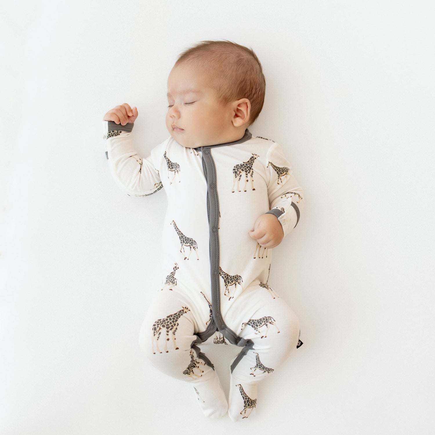 A sleeping baby wearing a Kyte Baby Snap Footie in the Giraffe print