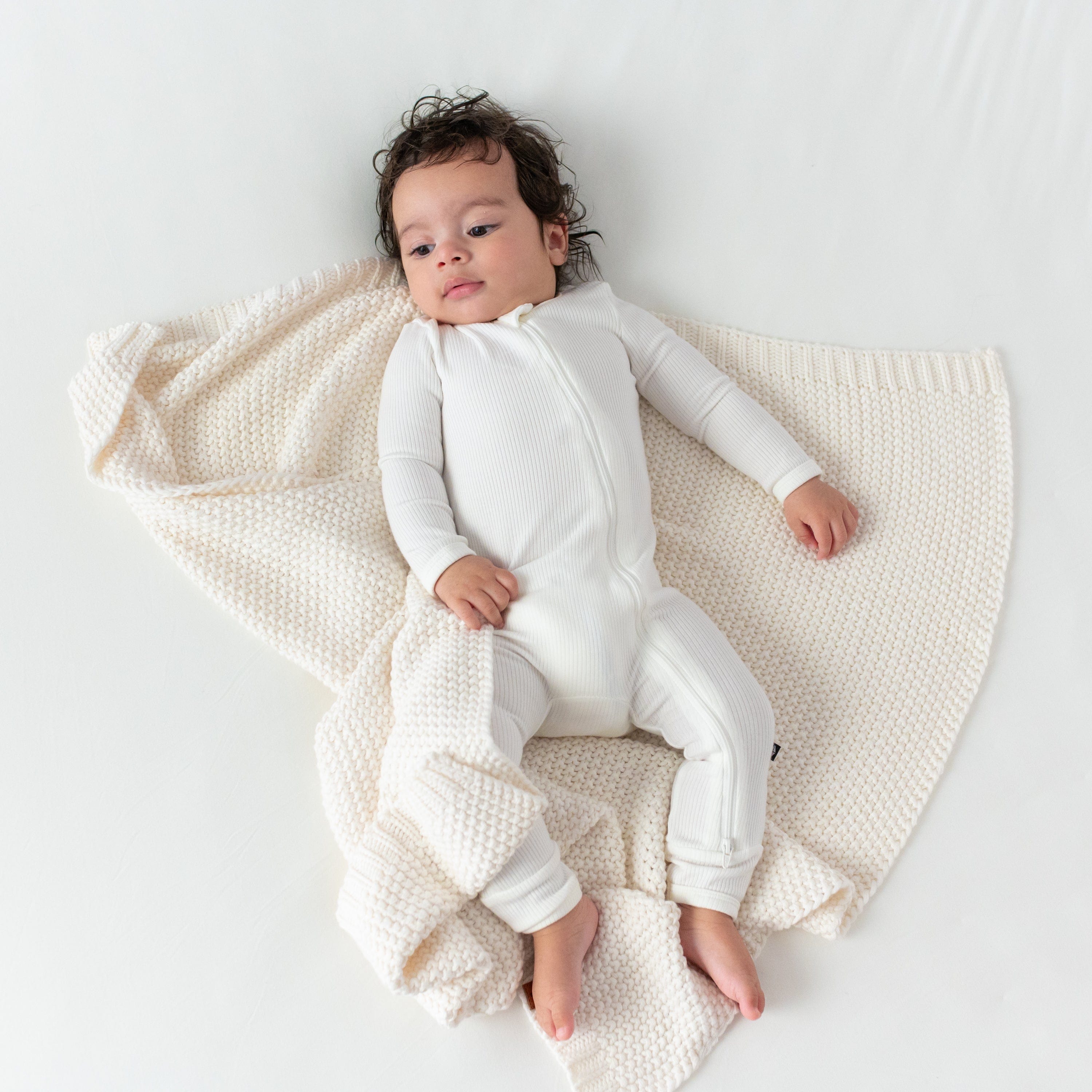 Infant in Ribbed Zippered Romper laying on Kyte Baby Chunky Knit Blanket