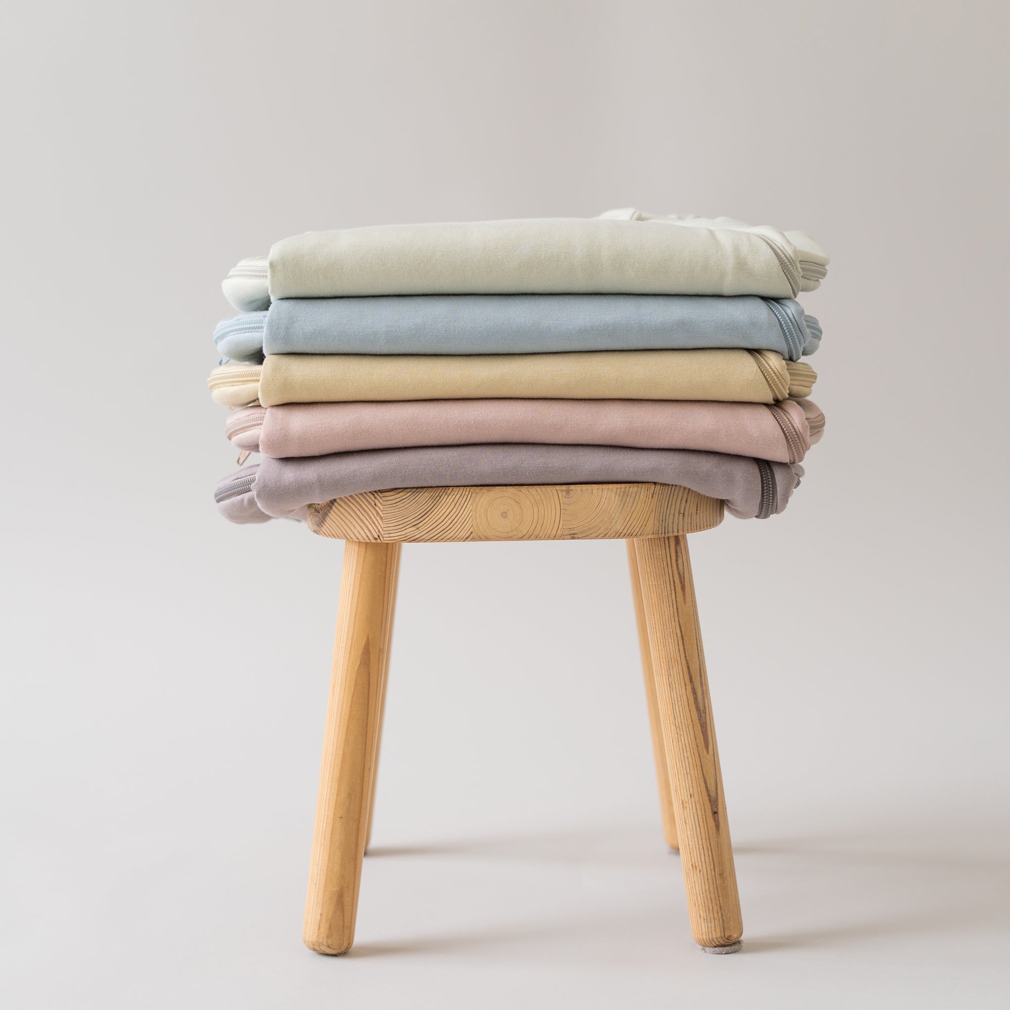 5 sleep bags folded on a stool in aloe, fog, wheat, sunset, mushroom