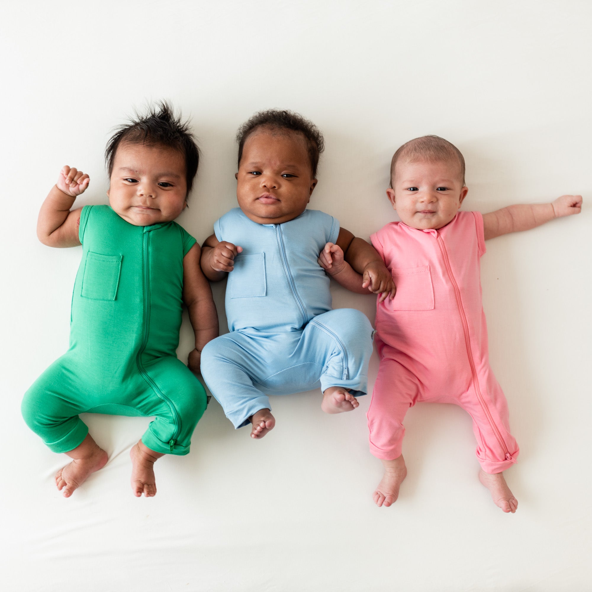 Three Babies Laying down wearing shortsleeve zippered rompers in fern, stream and rose