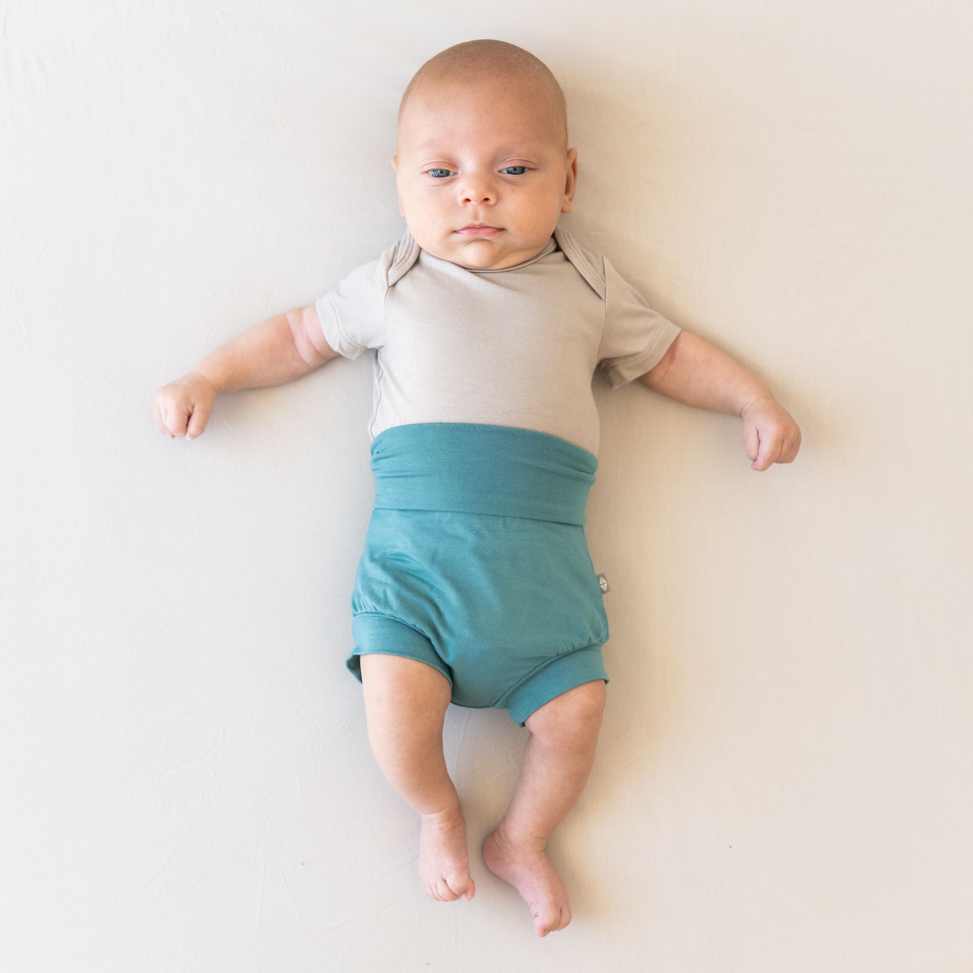 Baby laying down wearing bummies in the color cove