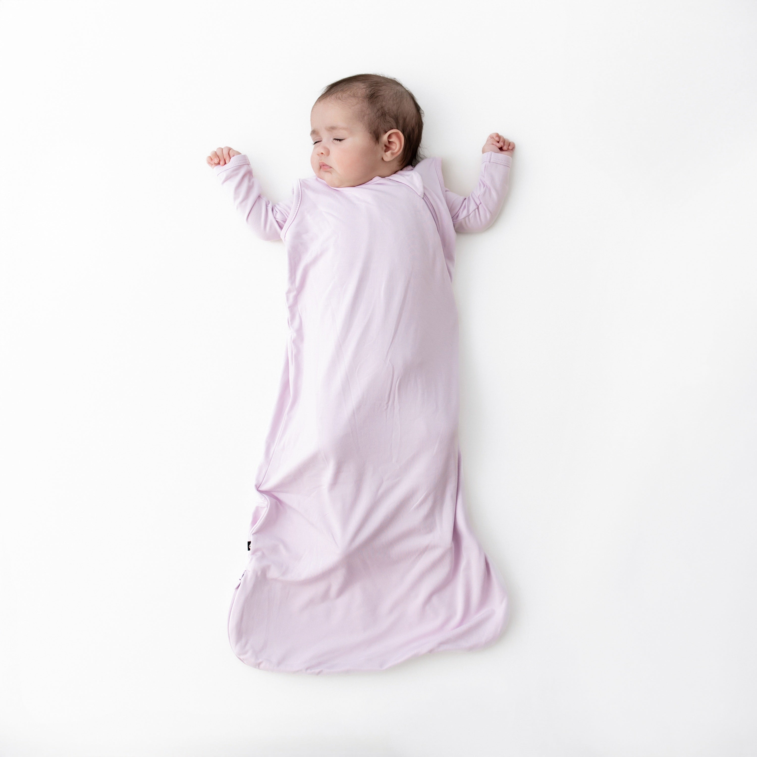 Sleeping infant wearing the Sleep Bag in Thistle 0.5 with matching romper on underneath