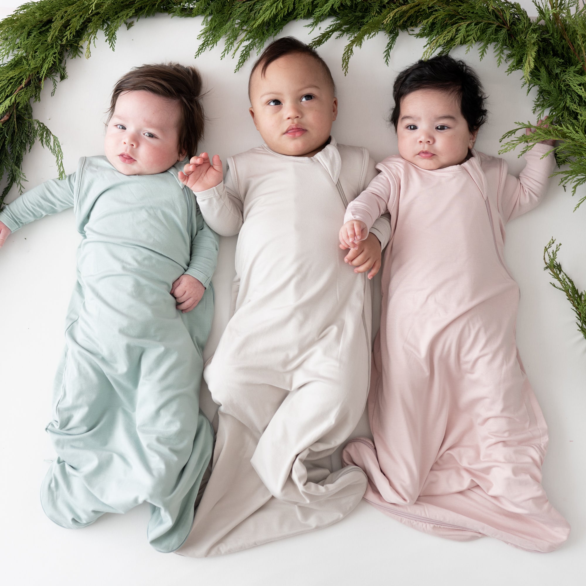 3 babies laying in 0.5 tog sleep bags in the colors sage, oat and blush