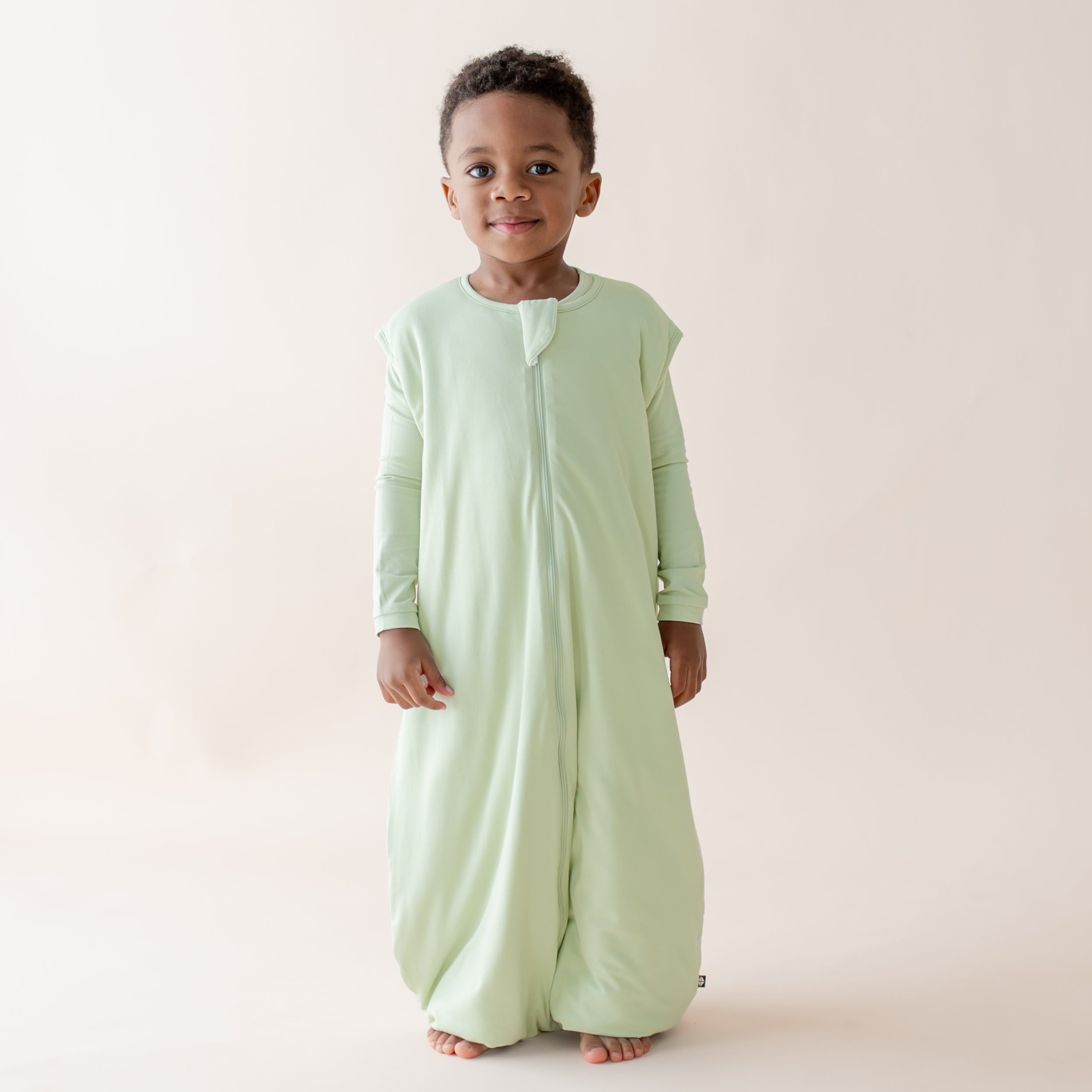 Child wearing a light green sleep bag walker against a plain background