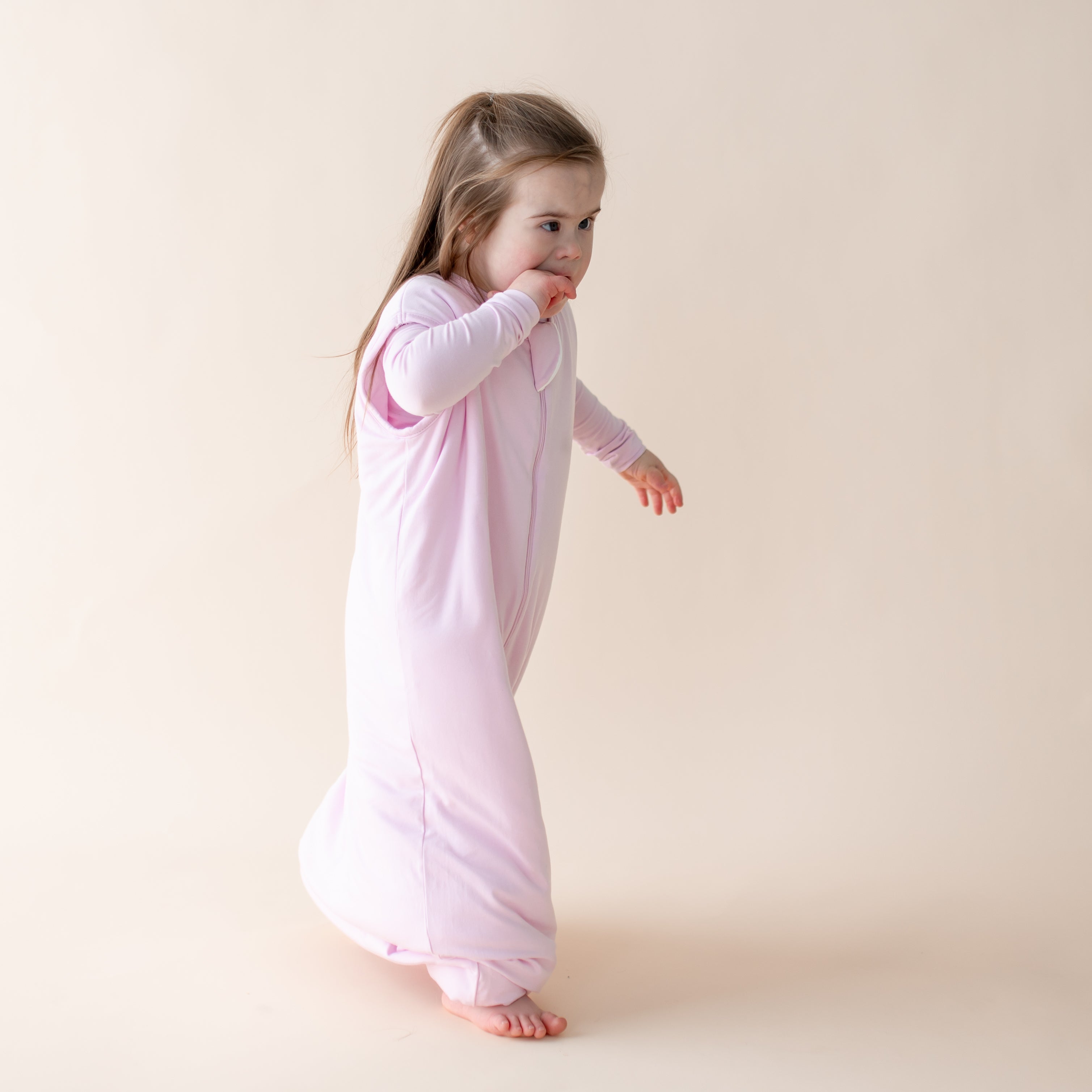 Young girl wearing a light purple sleep bag walker against a beige background