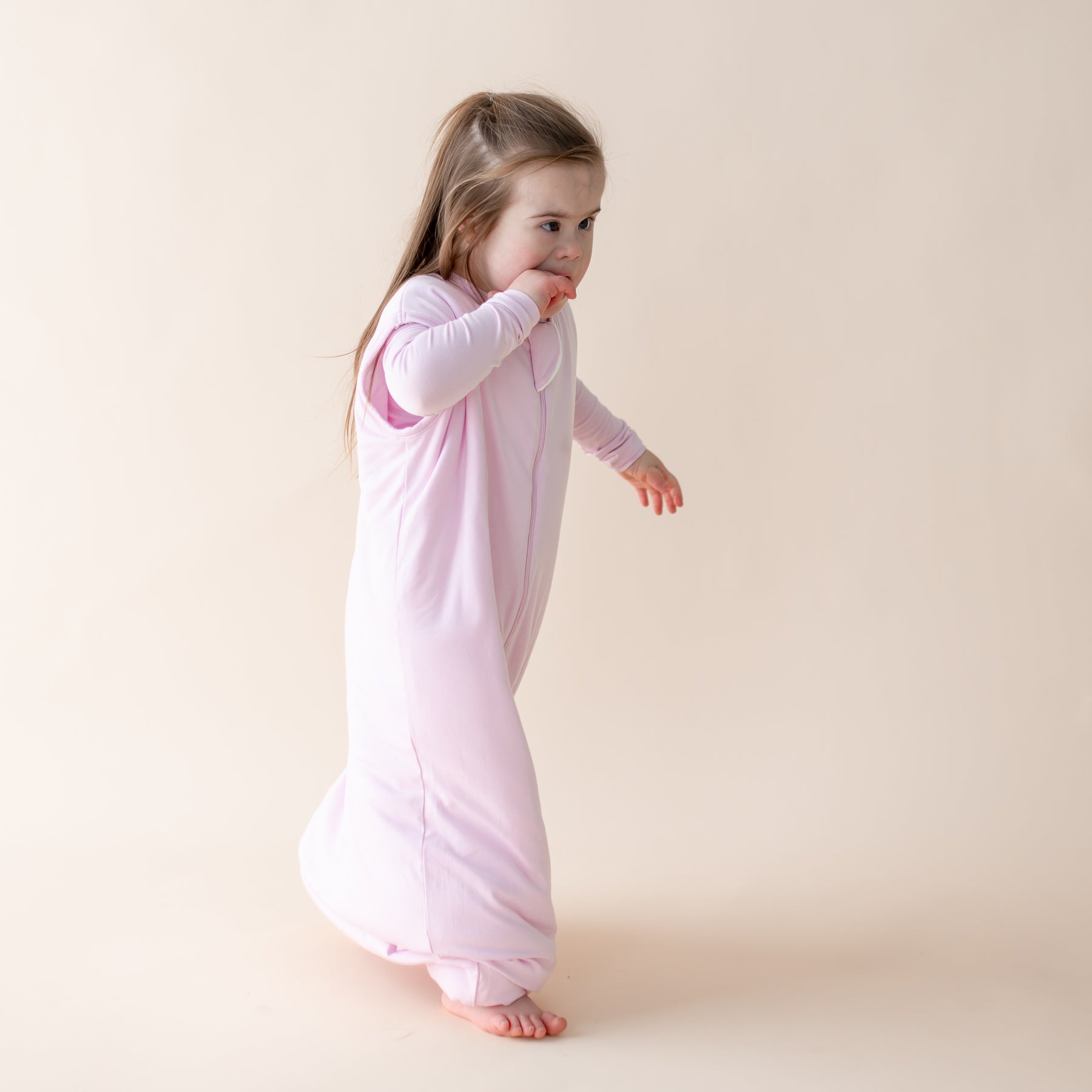 Young girl wearing a light purple sleep bag walker against a beige background