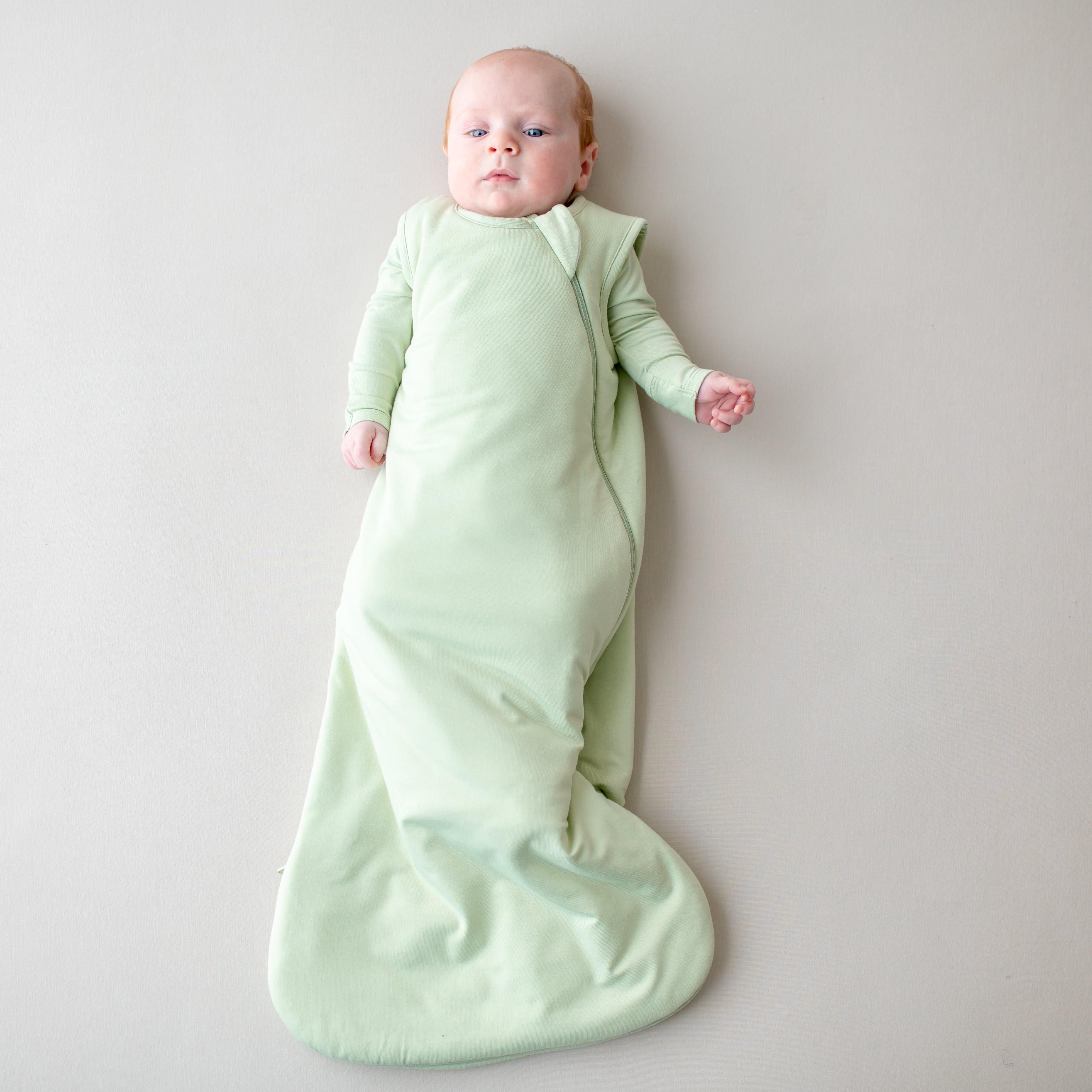 Baby in a 1.0 tog sleep bag in a light green color