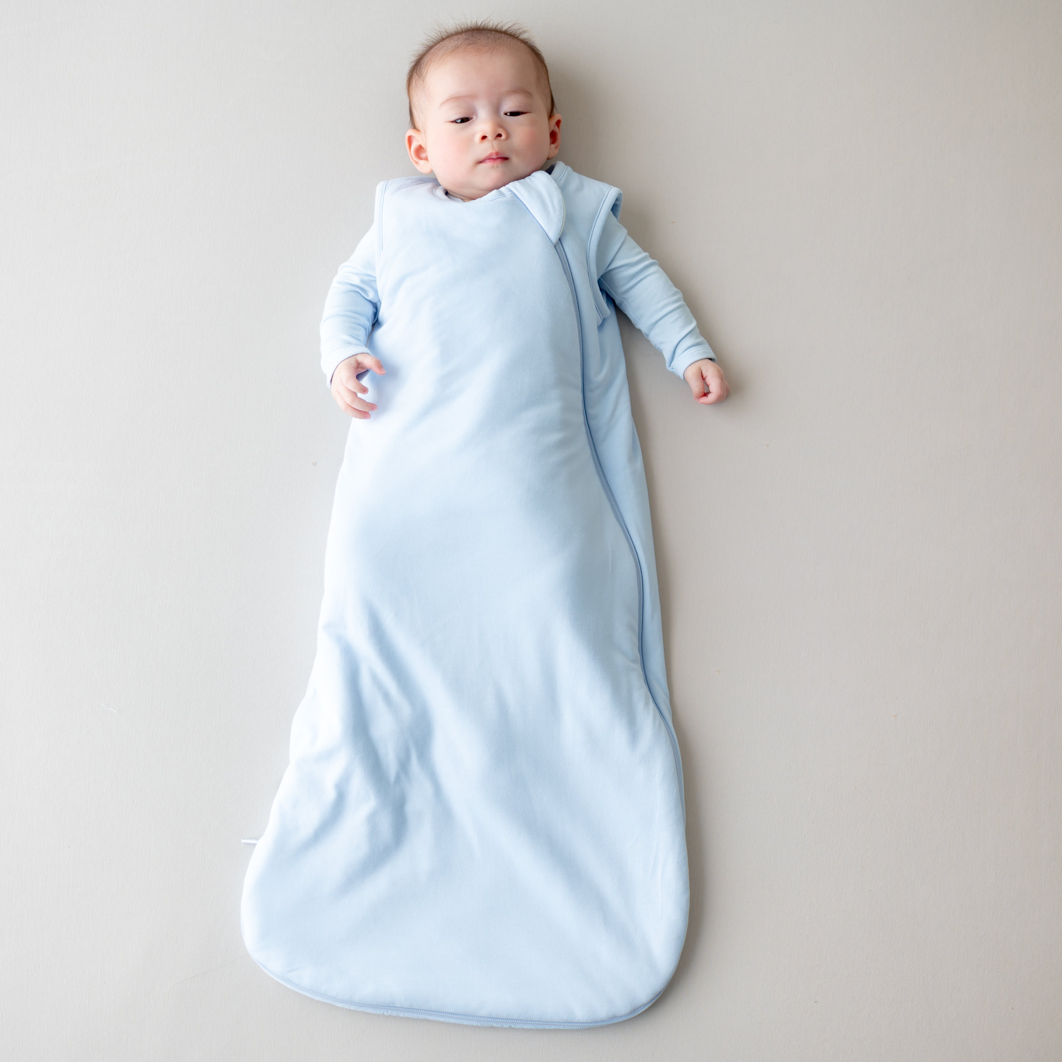 Baby wrapped in a light blue sleep bag on a neutral background
