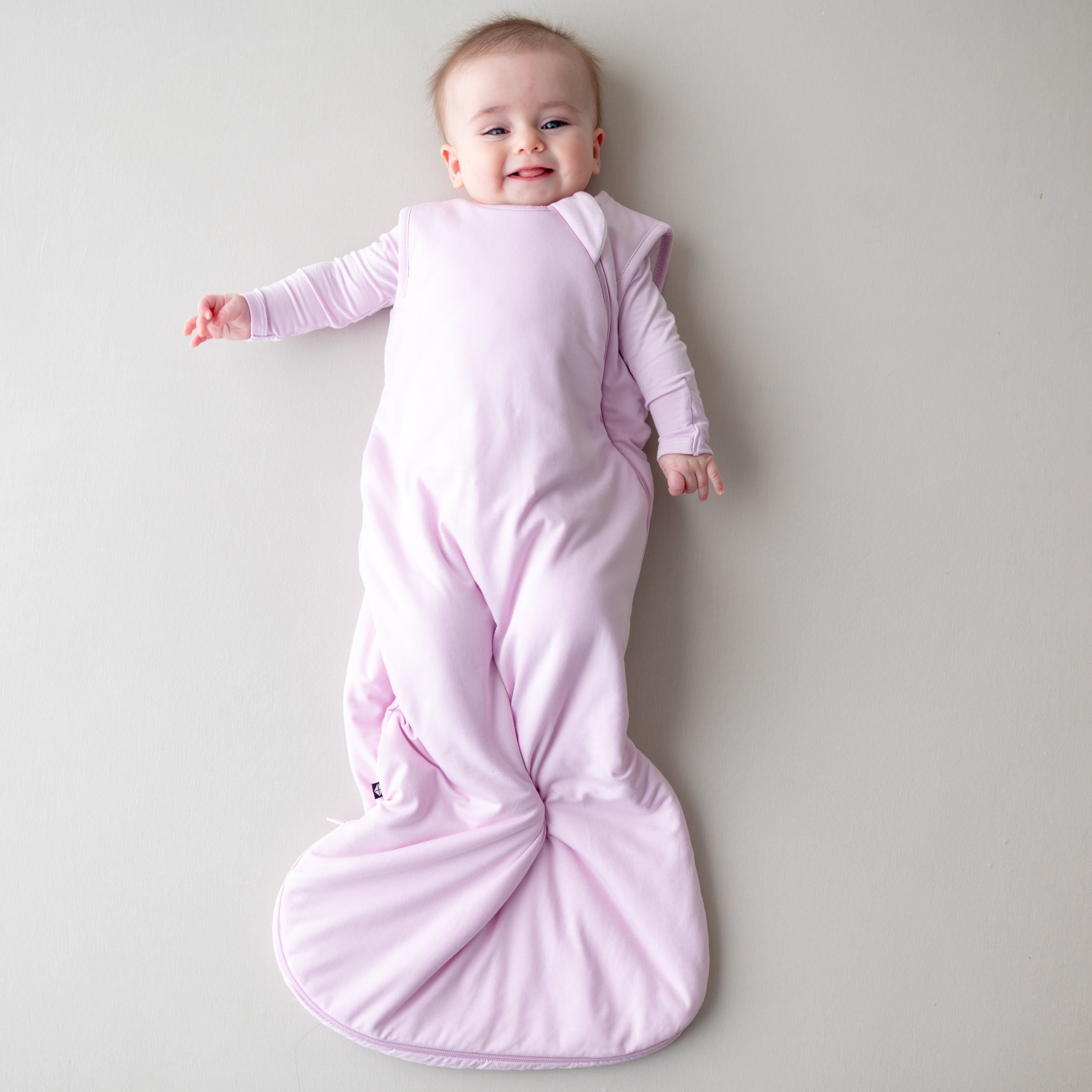 Baby wrapped in a light purple sleep bag on a plain background