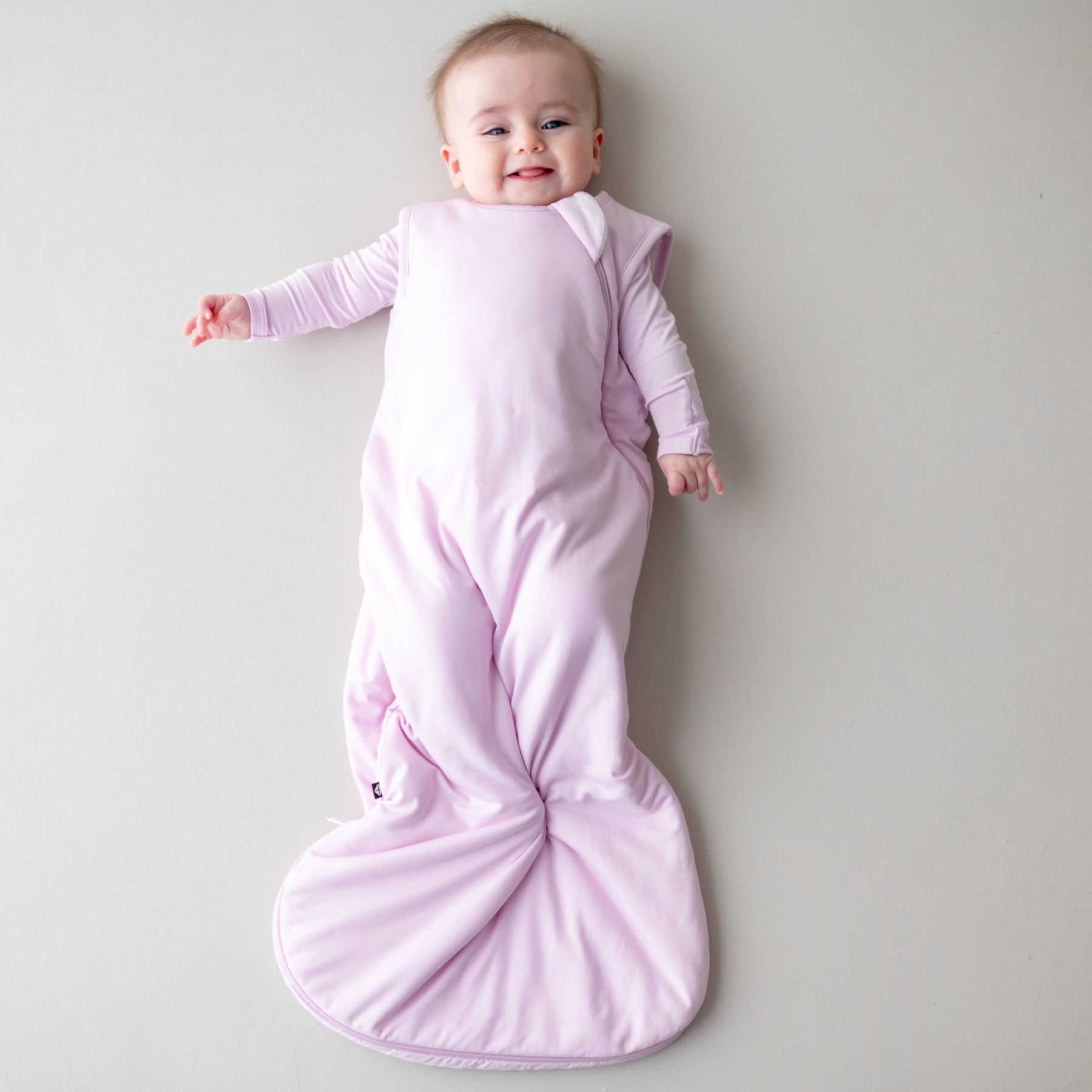 Baby wrapped in a light purple sleep bag on a plain background