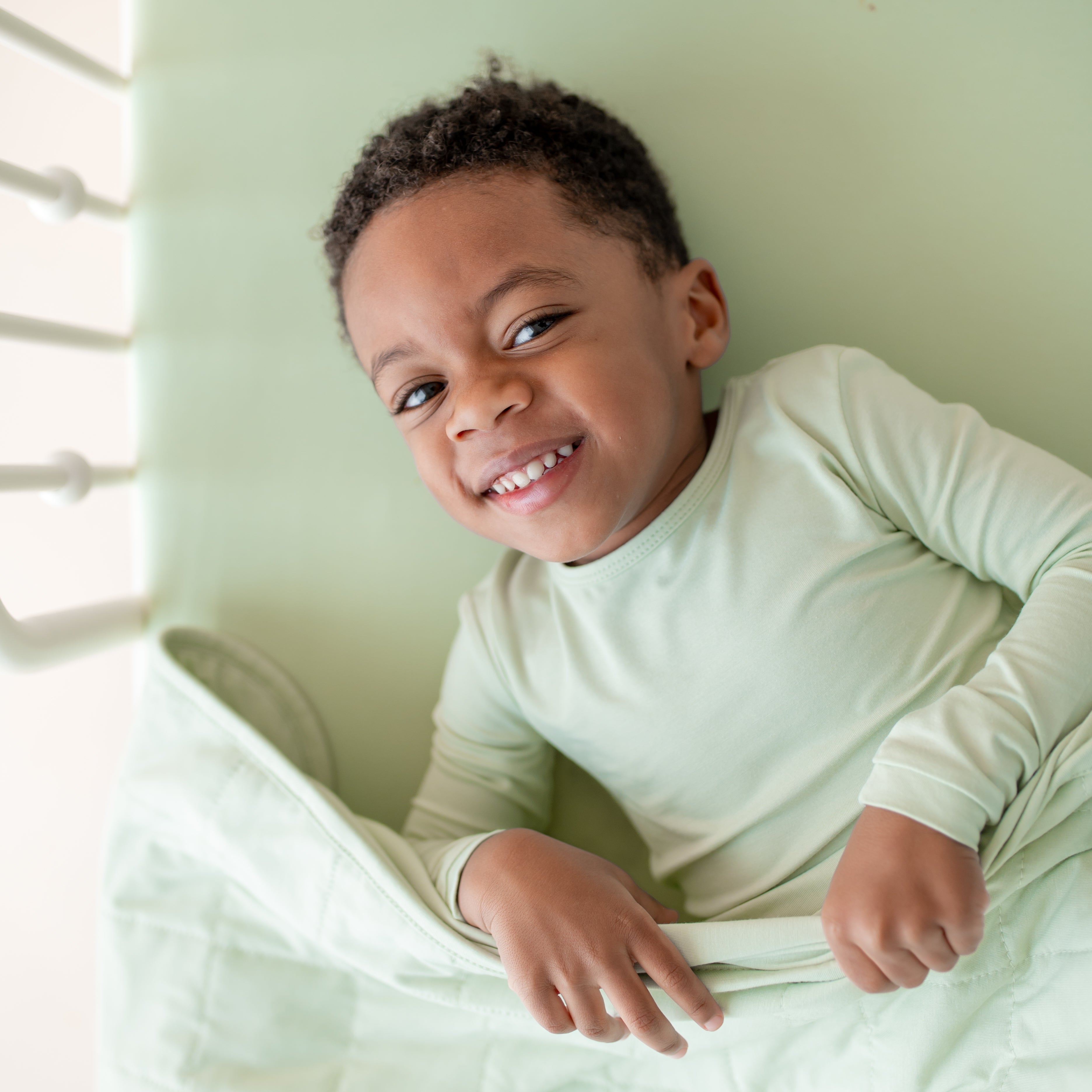 Child wearing light green pajama set laying on a bed with matching green bedding