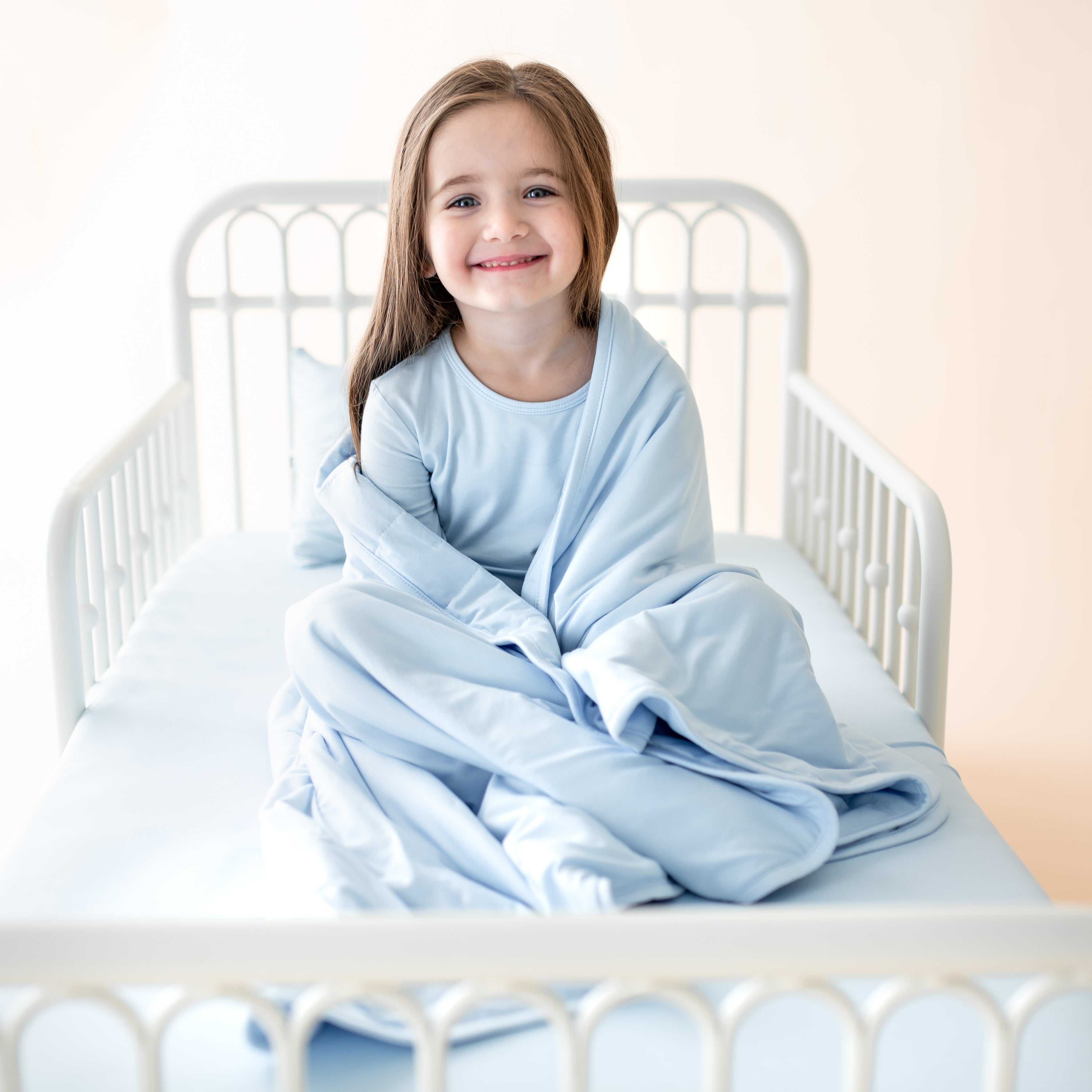 Toddler in a blue pajama set snuggling on a toddler bed with matching blue bedding