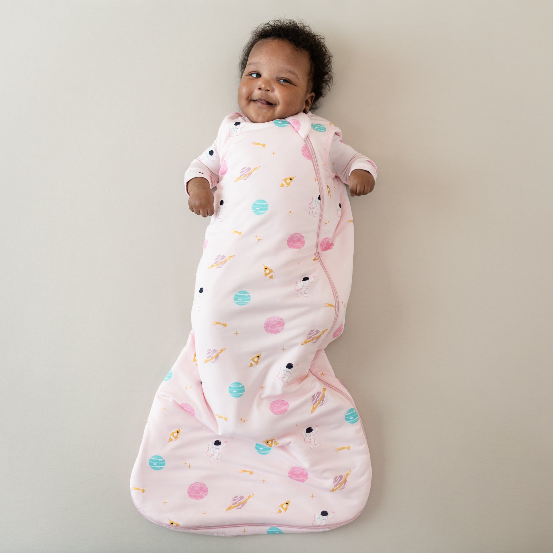 baby smiling and laying wearing sakura space sleep bag and footie