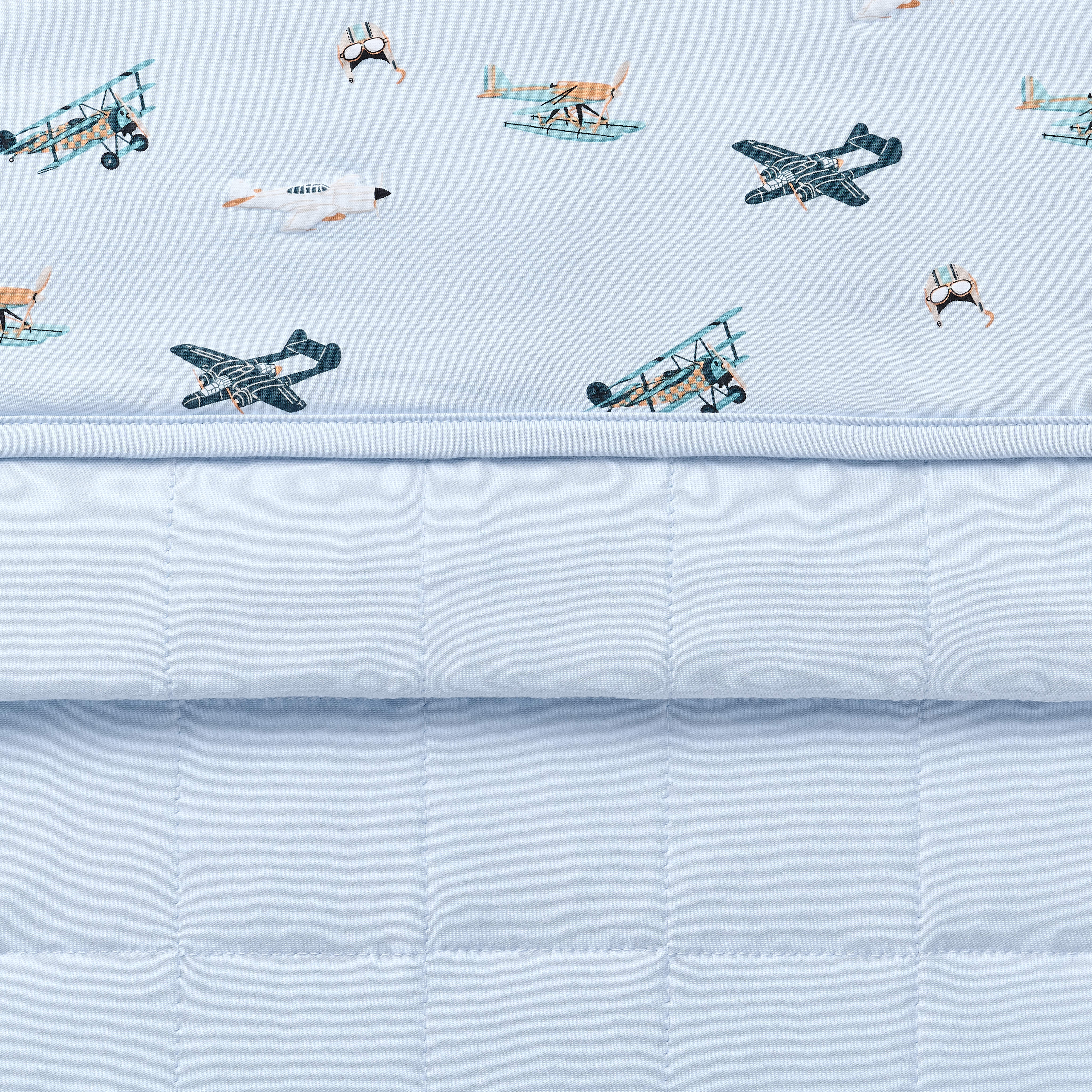 Close up of the Baby Blanket in Take Off showing the light blue quilted backing and plane patterned smooth top layer