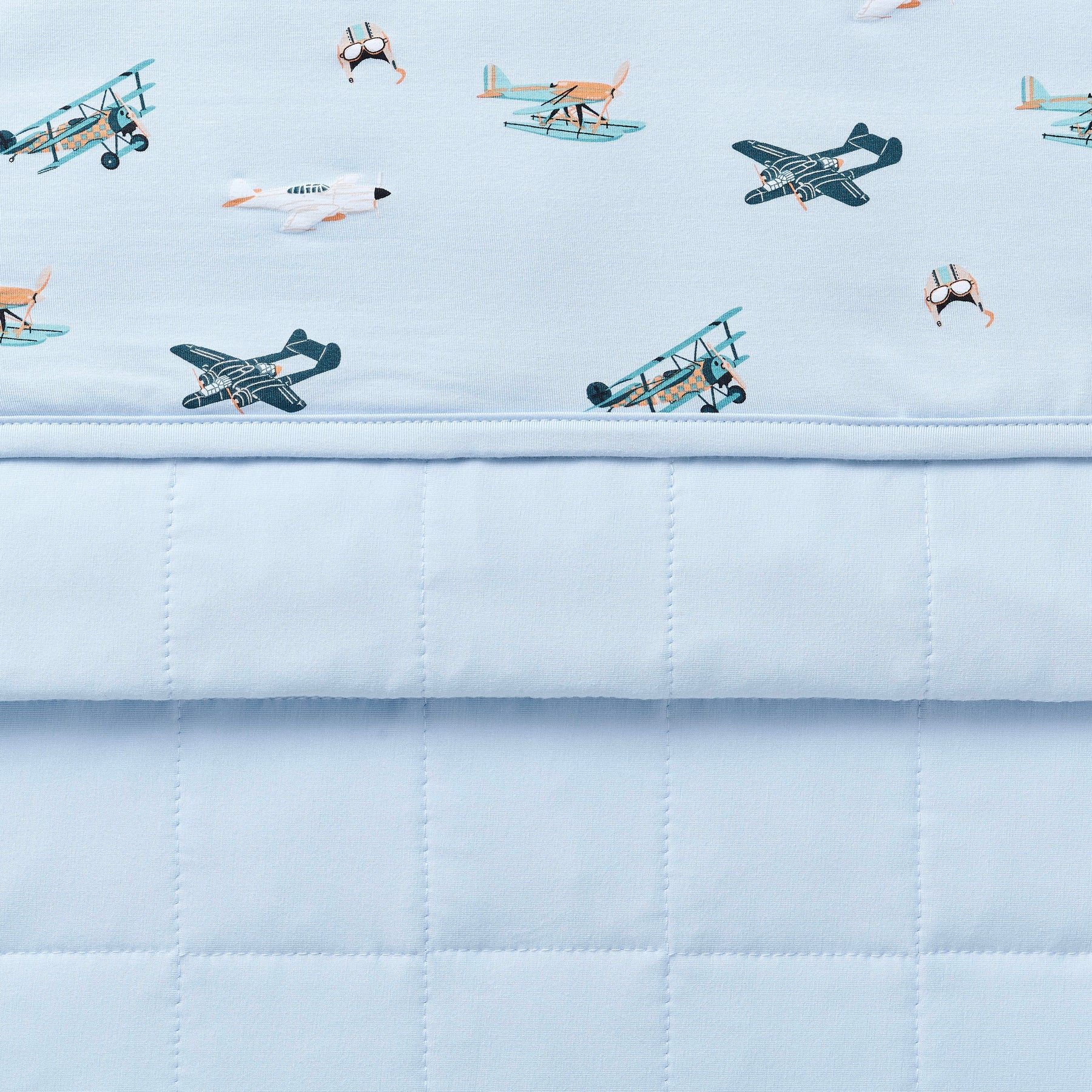 Close up of the Youth Blanket in Take Off 1.0 showing the baby blue quilted backing and plane print smooth top layer