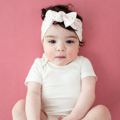 Baby wearing white onesie and knotted bow headband in pink bow print