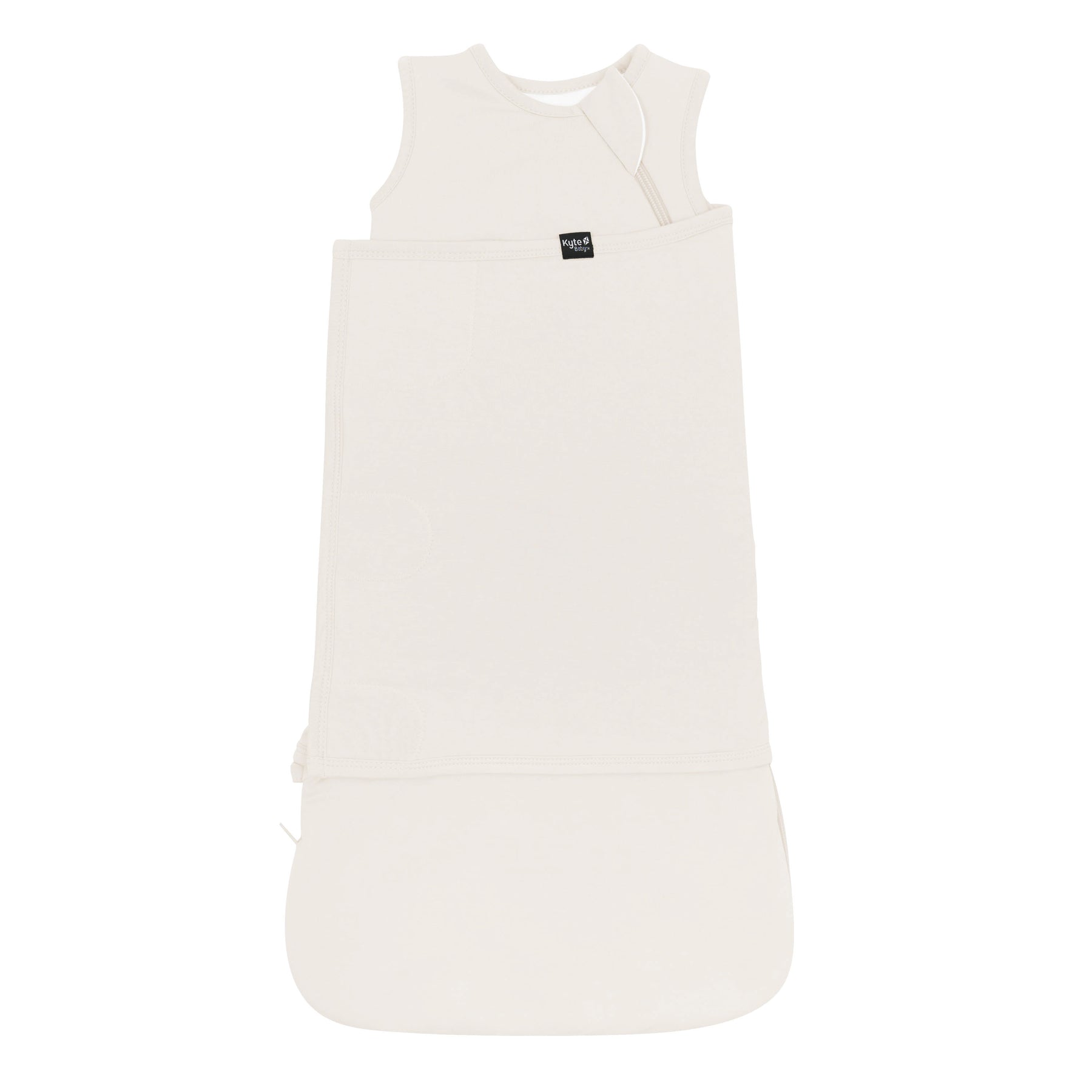 Sleep Bag Swaddler in Oat 1.0 shown swaddled with the Black Kyte Baby tag visible