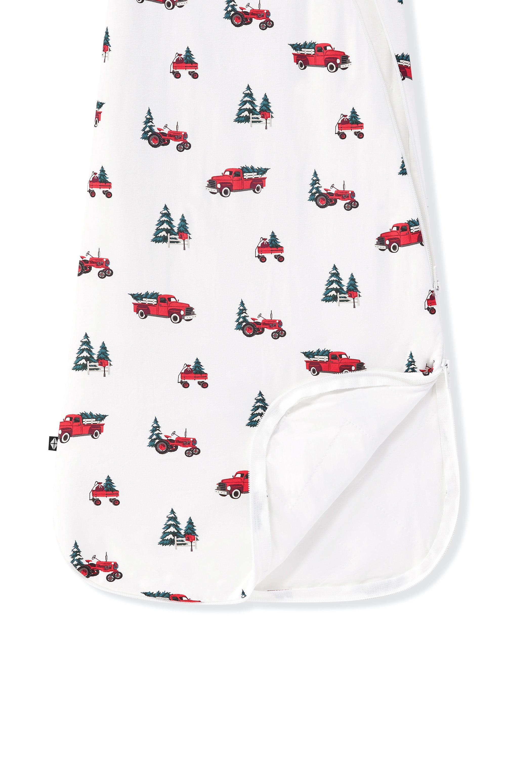 A close-up of a white baby blanket or swaddle with a repeating pattern of red pickup trucks carrying Christmas trees, with a folded-over corner showing a solid white reverse side.