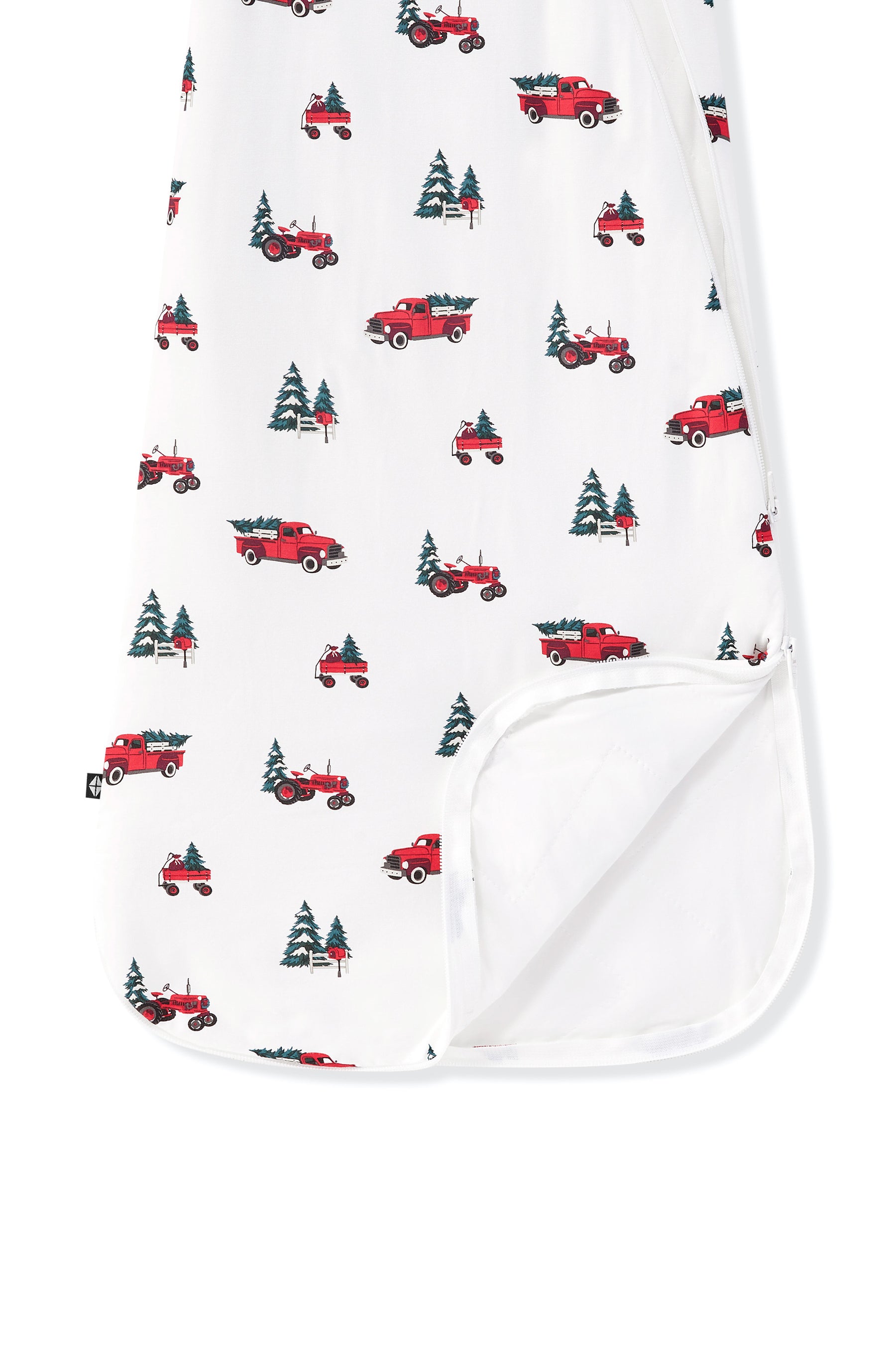 A close-up of a white baby blanket or swaddle with a repeating pattern of red pickup trucks carrying Christmas trees, with a folded-over corner showing a solid white reverse side.