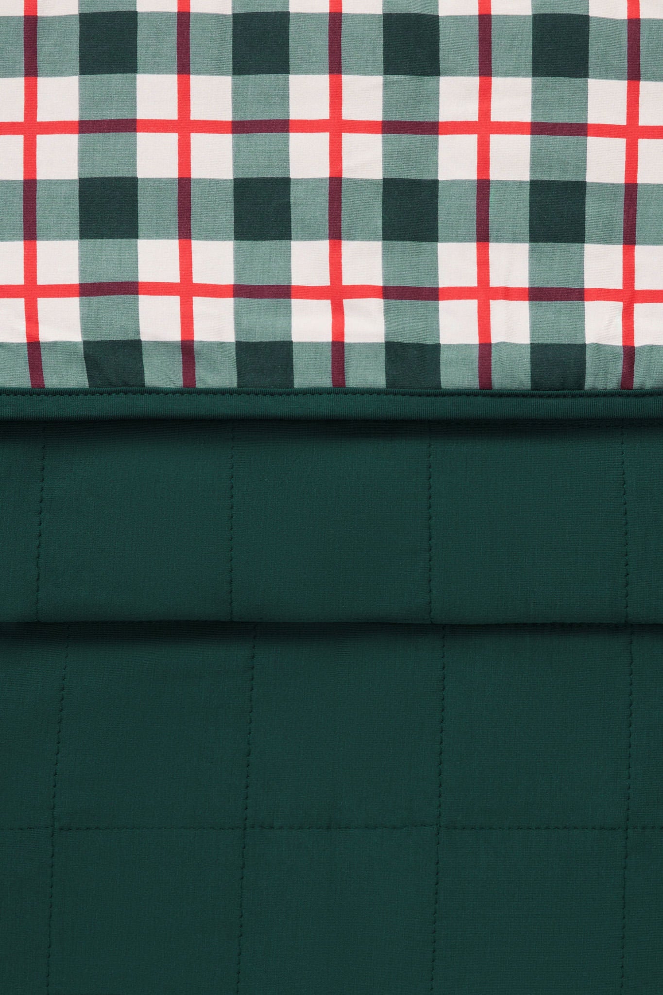 A close-up of a quilted fabric product showing two pattern sections: a dark green plaid top panel with white and red intersecting stripes, and a solid dark green quilted lower section.