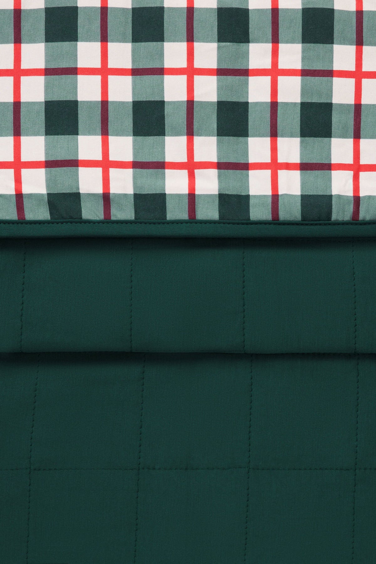 A close-up of a quilted fabric product showing two pattern sections: a dark green plaid top panel with white and red intersecting stripes, and a solid dark green quilted lower section.
