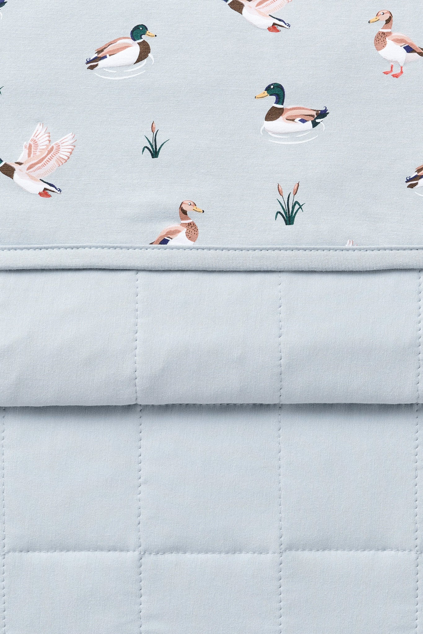 Close up of the Youth Blanket in Mallard Duck 1.0 showing the light blue quilted backing and patterned smooth top layer