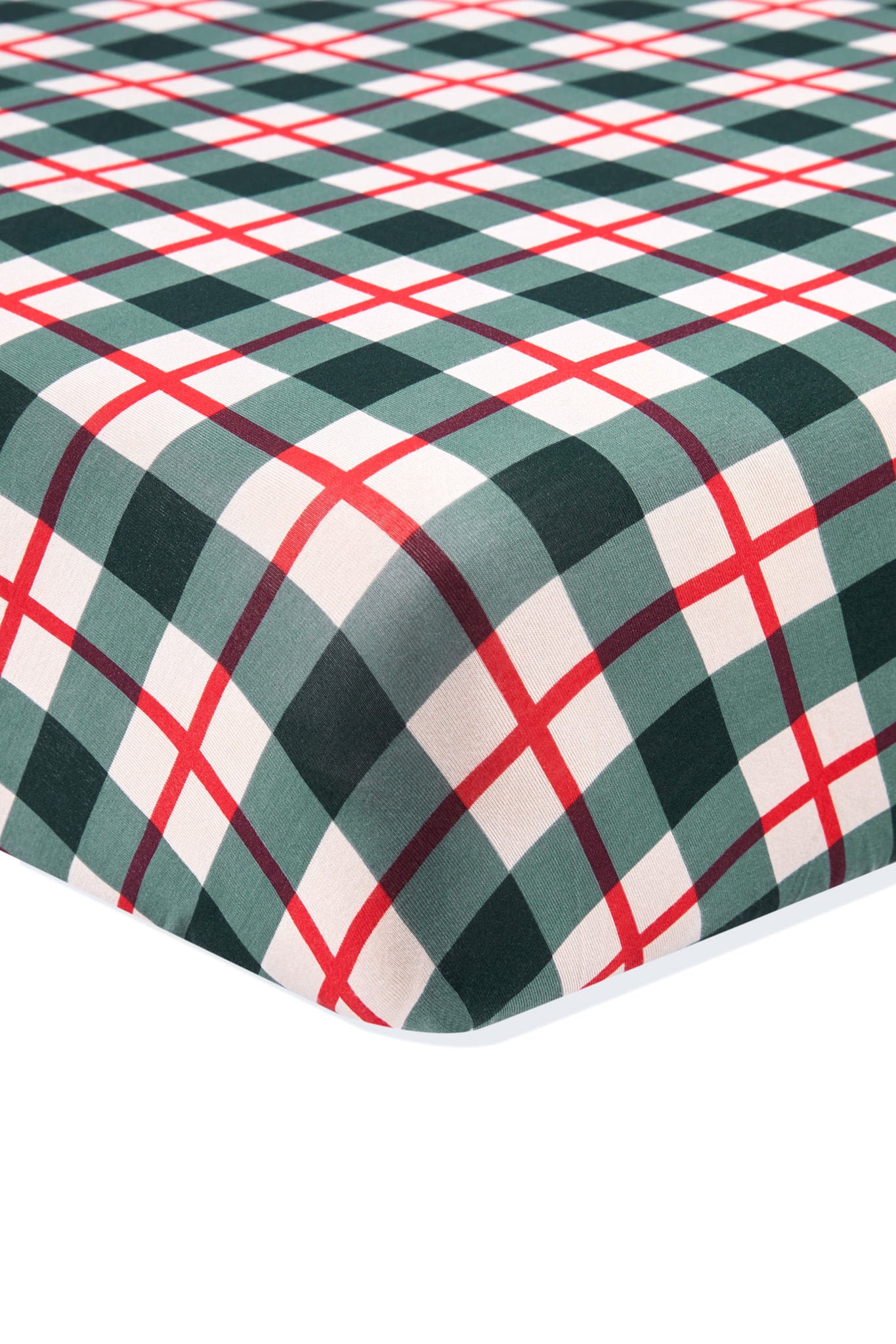 A close-up of a plaid fabric surface, likely a fitted sheet or blanket, featuring a green, white, and red tartan pattern on a white background.