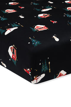 A close-up of a fitted sheet or mattress cover with a black background and a festive Christmas print featuring red and white campers, snowmen, evergreen trees, and snowflakes.