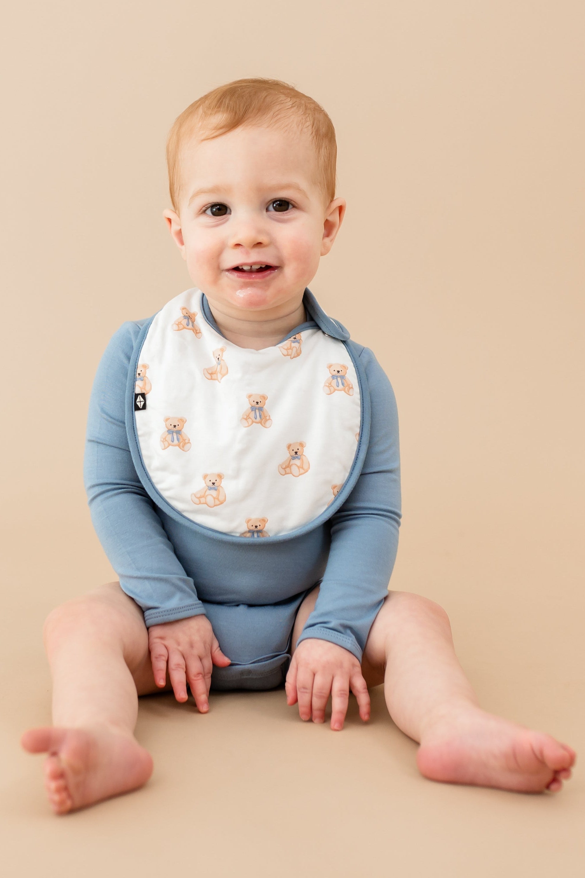 Young toddler wearing Cushy Bib in Teddy Bear with slate bodysuit 