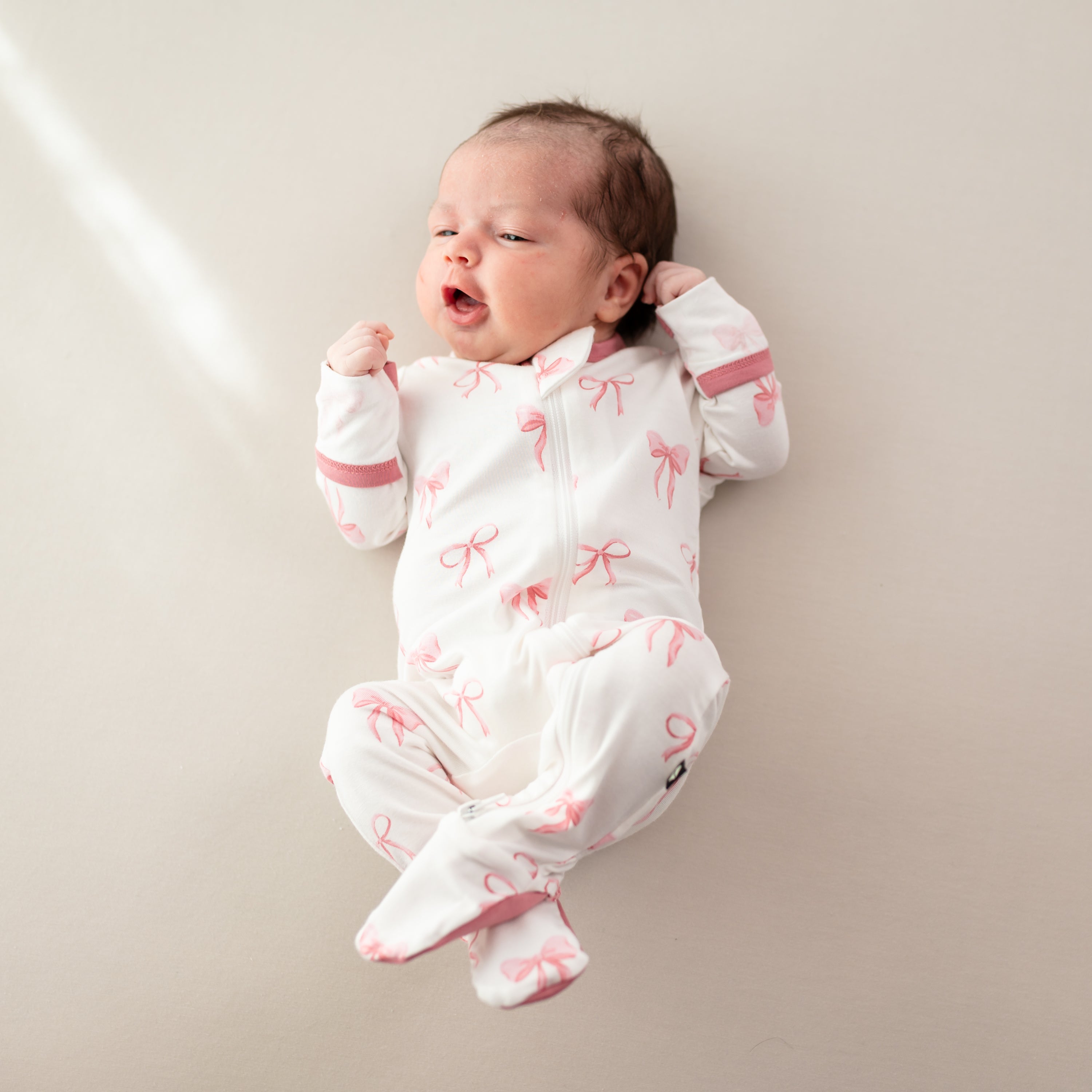 Baby wearing Zippered Footie in pink Bow print