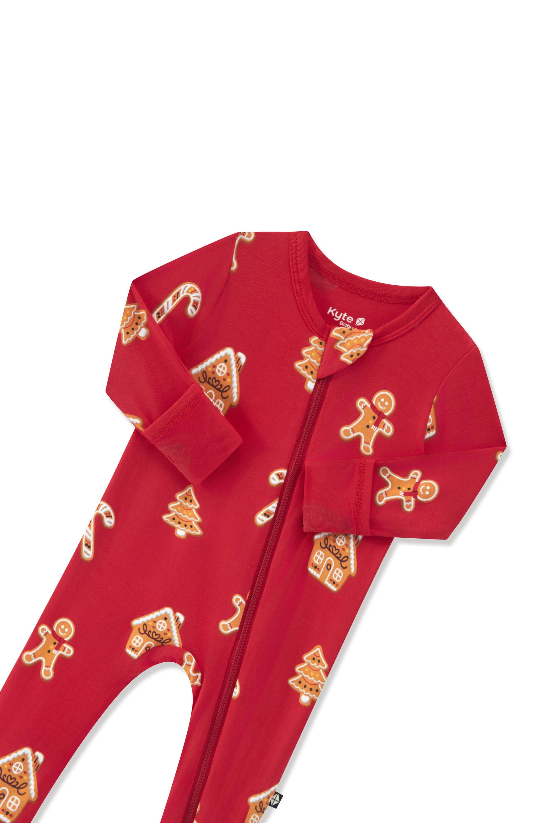A red long-sleeve baby footed sleeper with a front zipper, featuring an all-over gingerbread-themed print of gingerbread men, houses, and candy canes, shown on a plain white background.