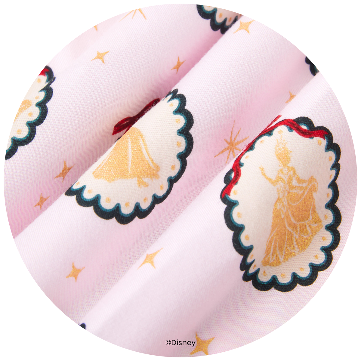 A close-up circular view of a light pink fabric with a repeating print of Disney princess dresses in gold, outlined in black and blue, with small gold stars.