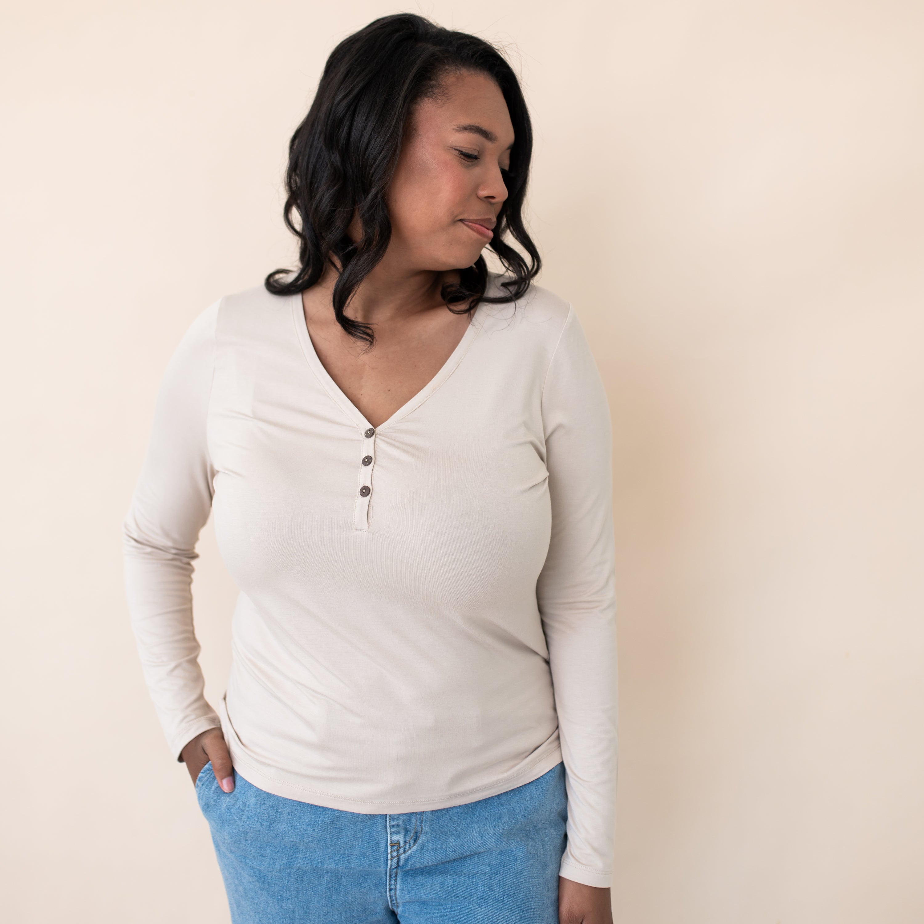 Female model looking over her shoulder wearing the Women's Long Sleeve Henley Tee in Bisque
