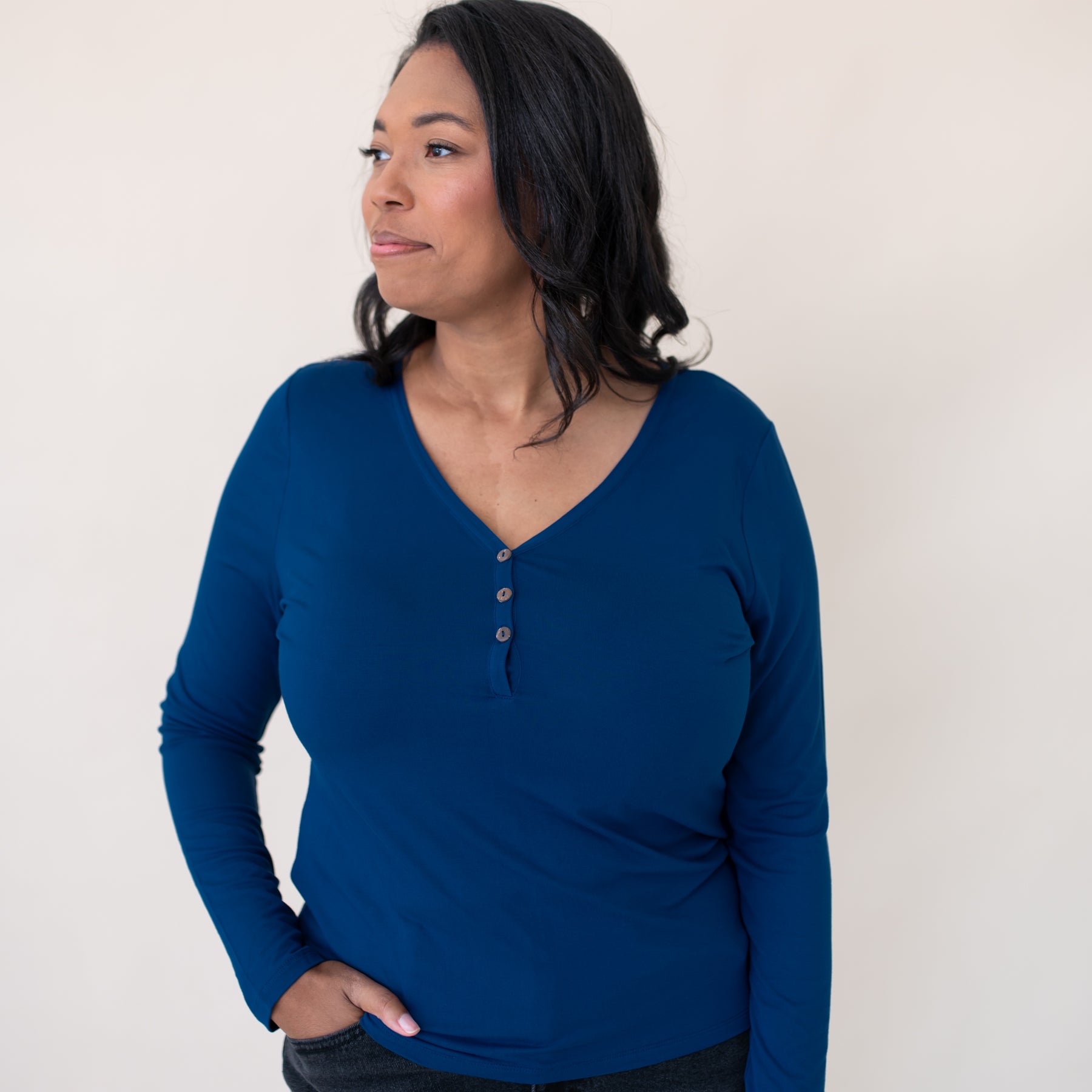 Female model standing wearing the Women's Long Sleeve Henley Tee in Tahoe paired with dark wash jeans