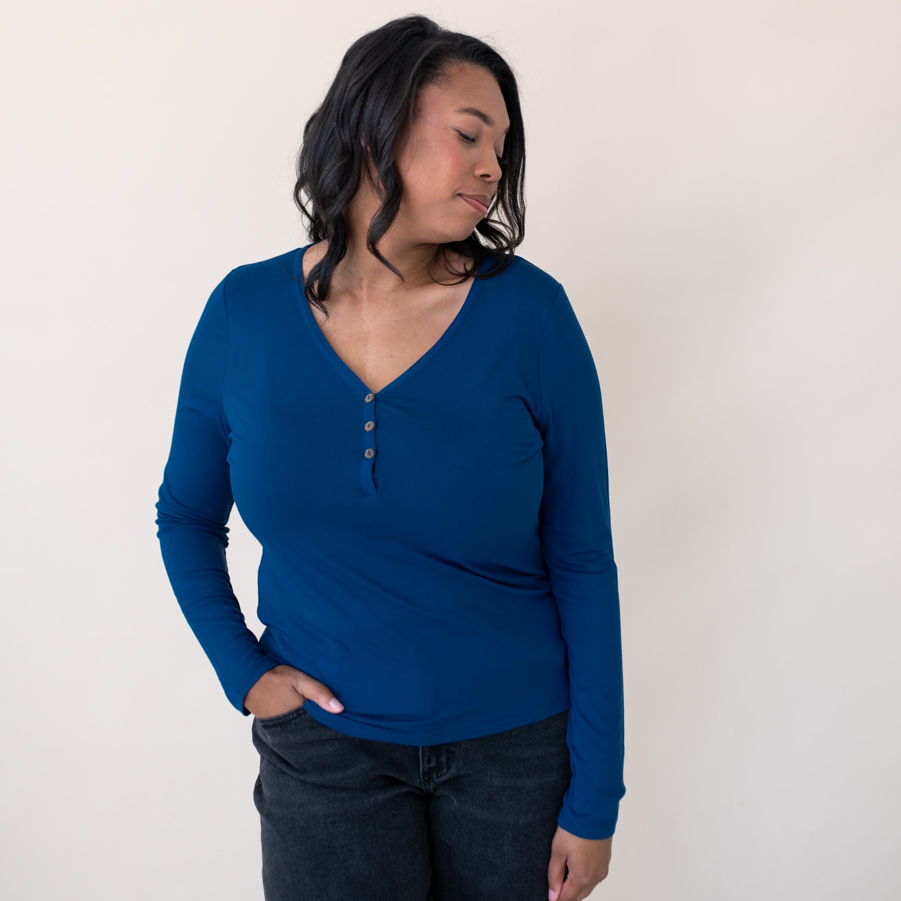 Female model looking over her shoulder wearing the Women's Long Sleeve Henley Tee in Tahoe with dark wash jeans